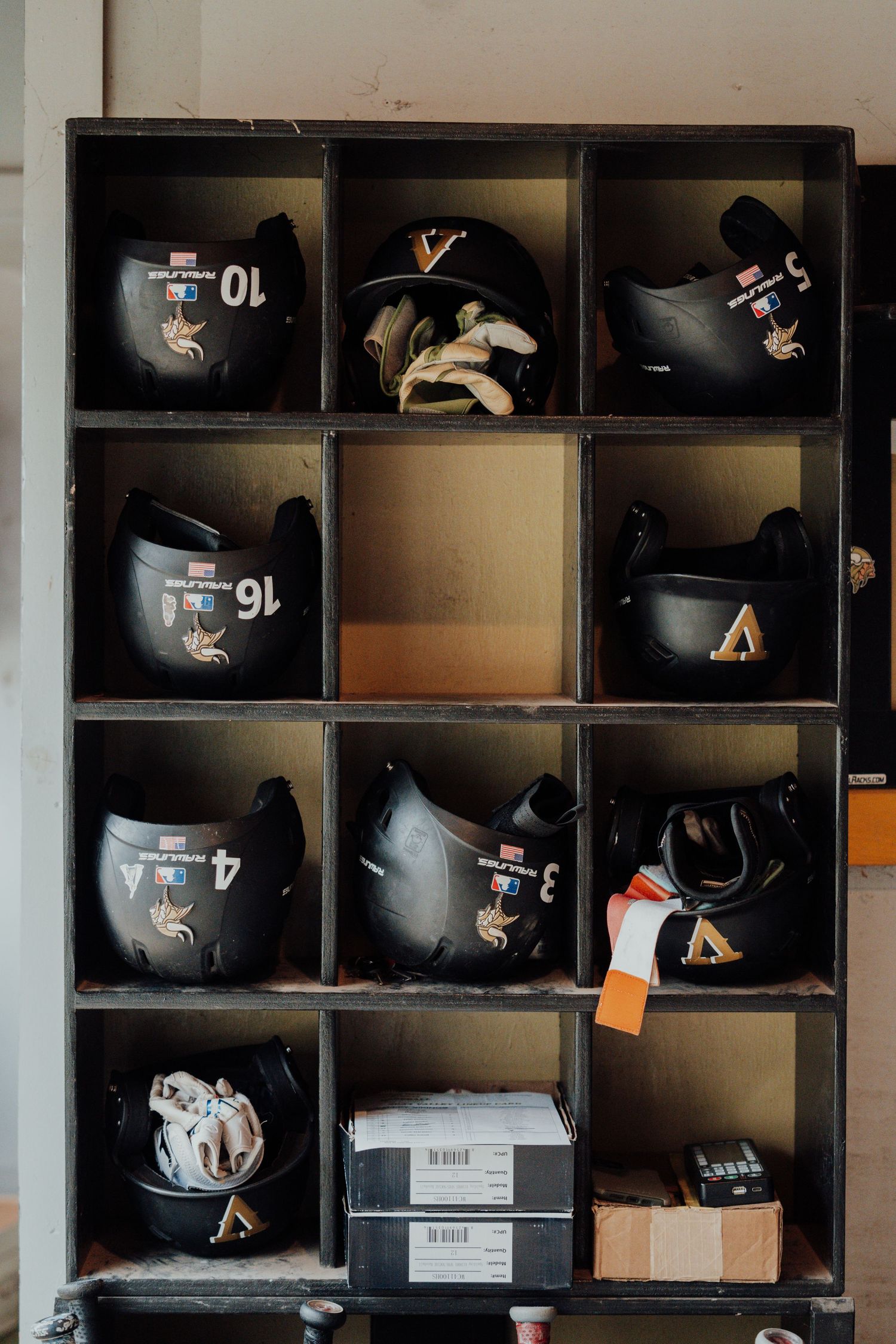 Baseball helmets arranged in organized storage cubbies with team uniform numbers visible.
