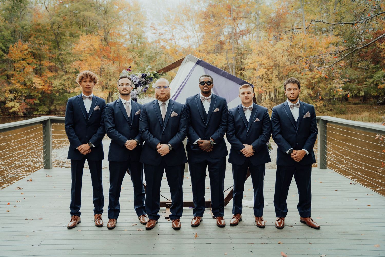 A wedding party in navy suits standing on a wooden bridge during fall.