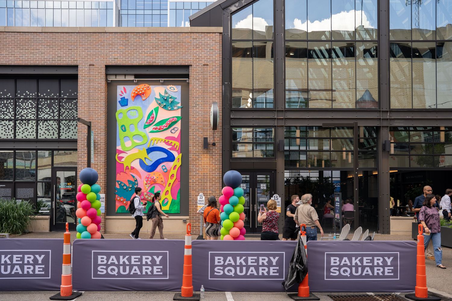Colorful balloon decorations and vibrant mural adorn the entrance of Bakery Square with pedestrians walking past.