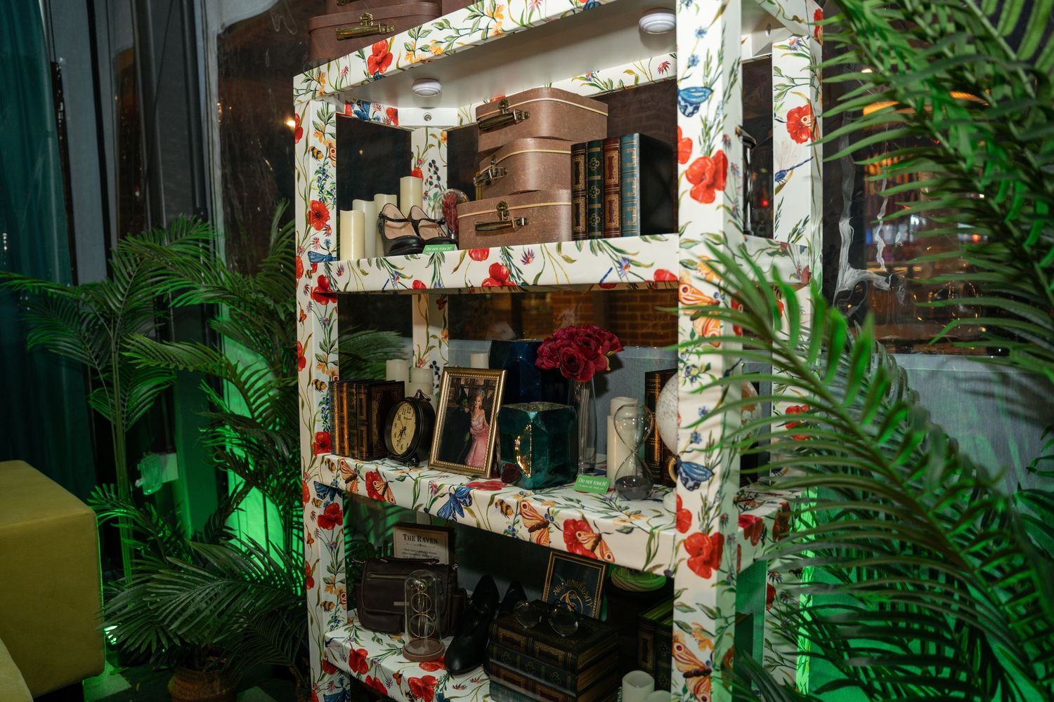 Retail display shelf decorated with floral patterns and surrounded by tropical plants with green lighting.