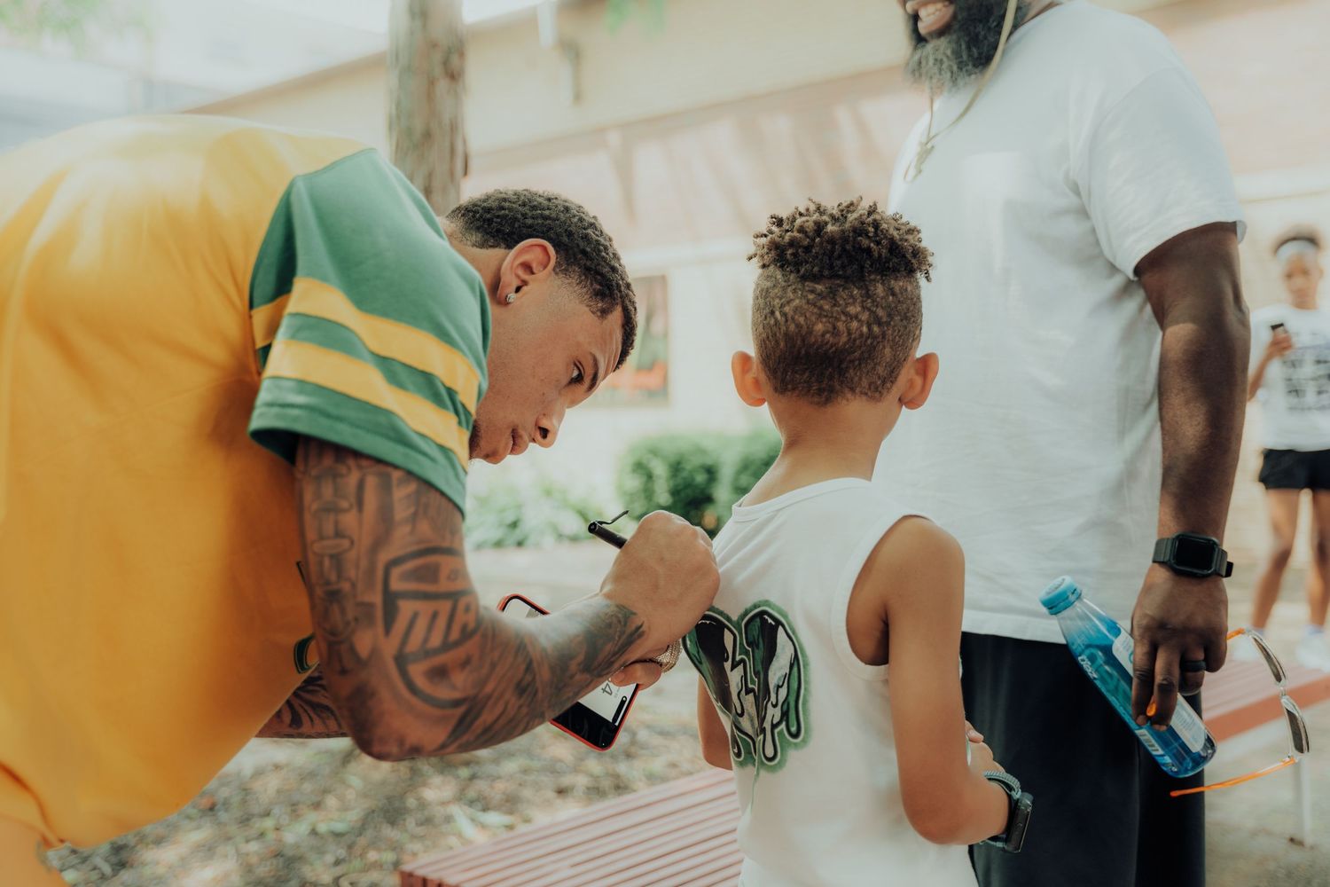 Person in yellow shirt is seen interacting with a child wearing a white tank top outdoors on a summer day.