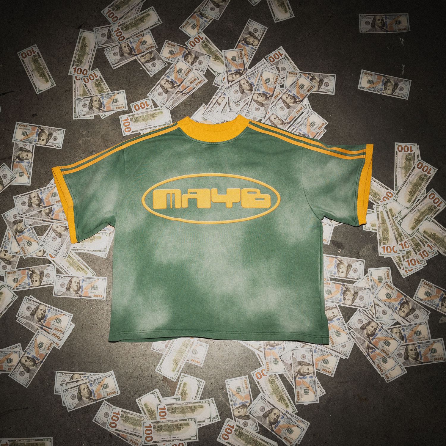 Green and yellow vintage-style t-shirt surrounded by scattered dollar bills on dark surface.