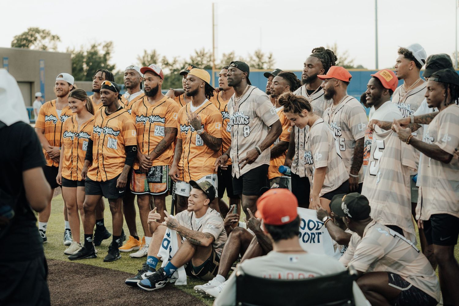 A group of baseball players and supporters gather together on a field wearing orange jerseys and casual attire.