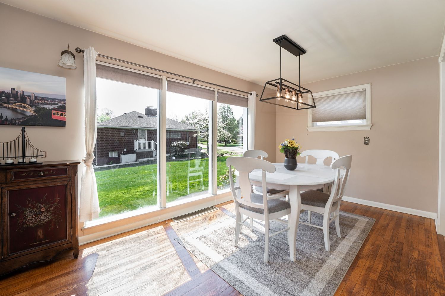 Modern dining room features hardwood floors, white walls, and large windows offering natural light and scenic views.