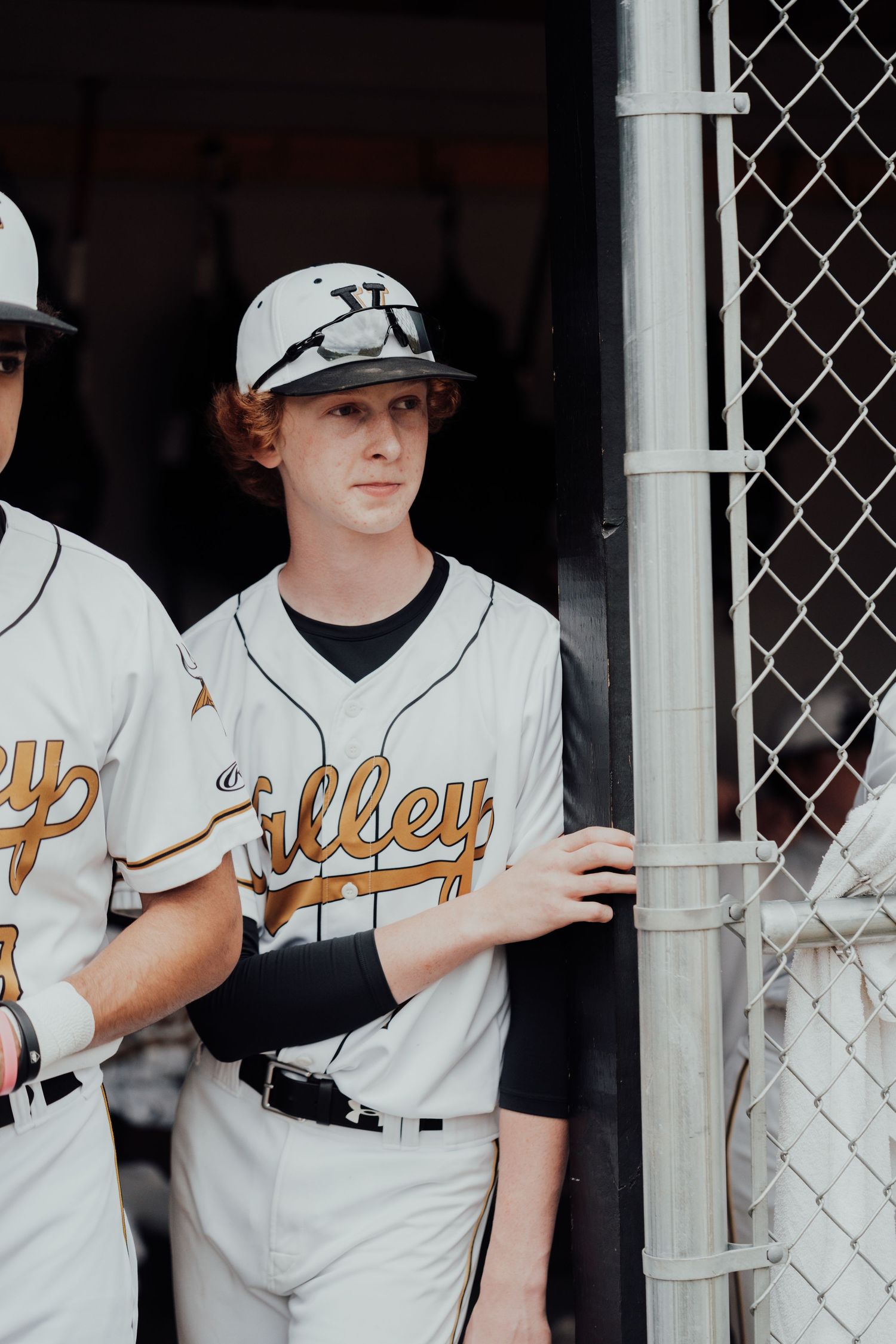 Baseball team members in white Valley jerseys line up against dugout fence.