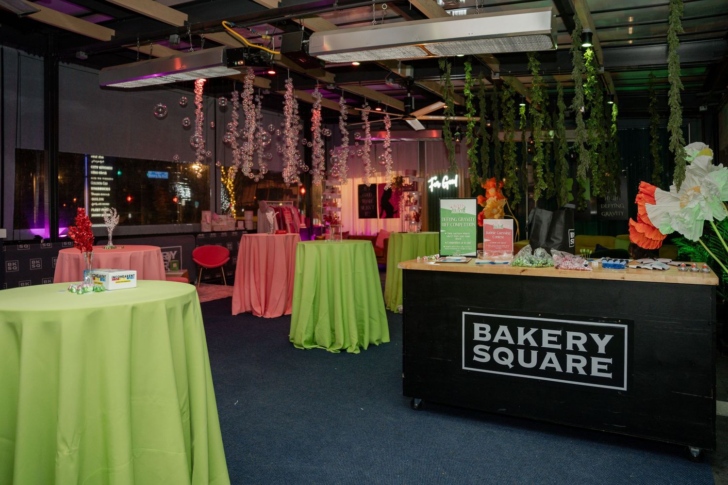 Corporate event setup at Bakery Square with lime green tablecloths and hanging floral decorations under mood lighting.