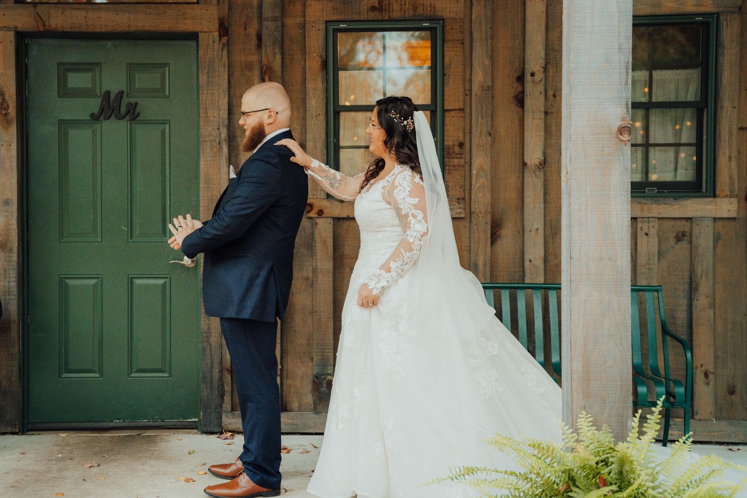 A rustic wedding first look scene with green doors and wooden walls.