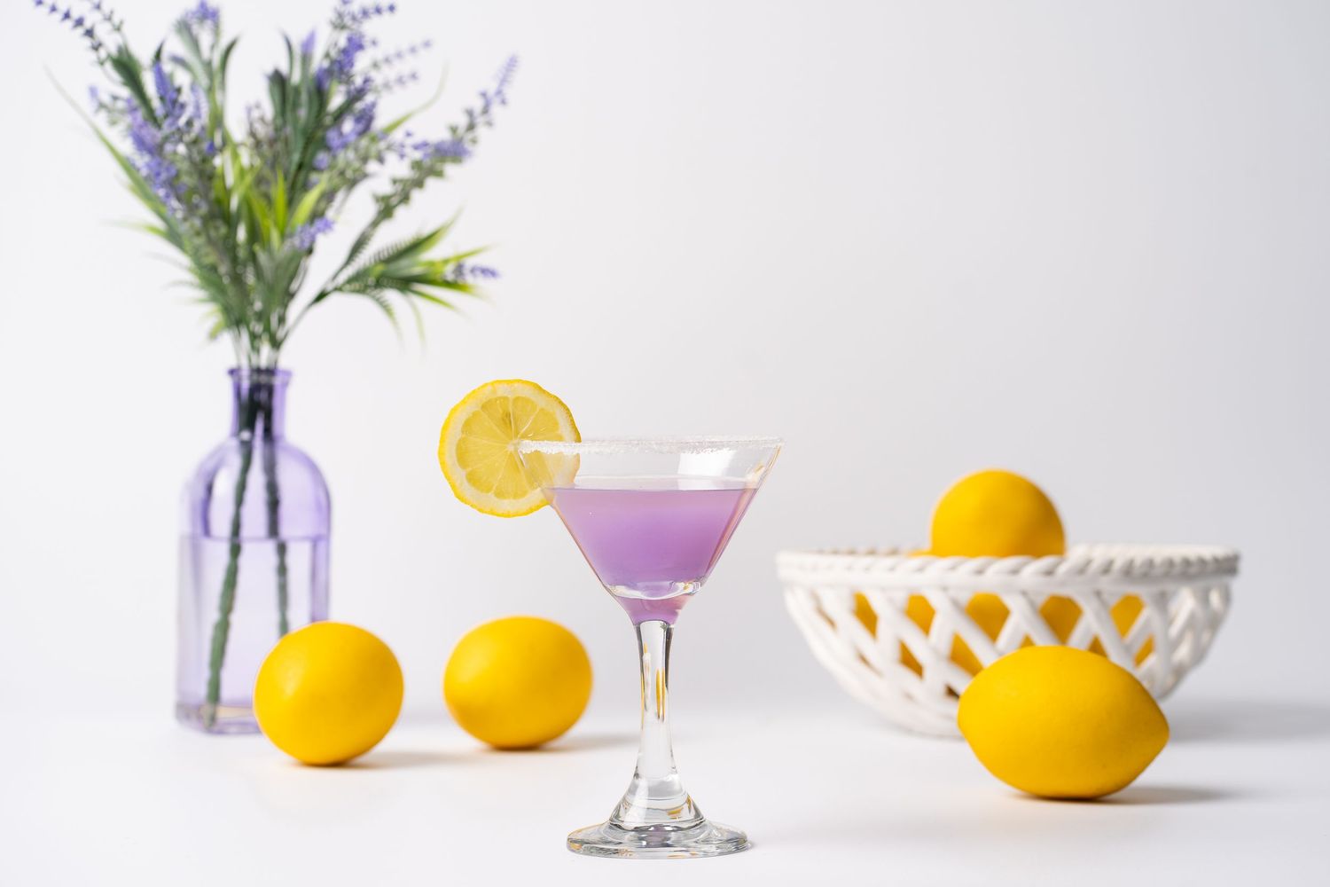 Citrus cocktail styling with fresh lemons and purple flowers against white backdrop.