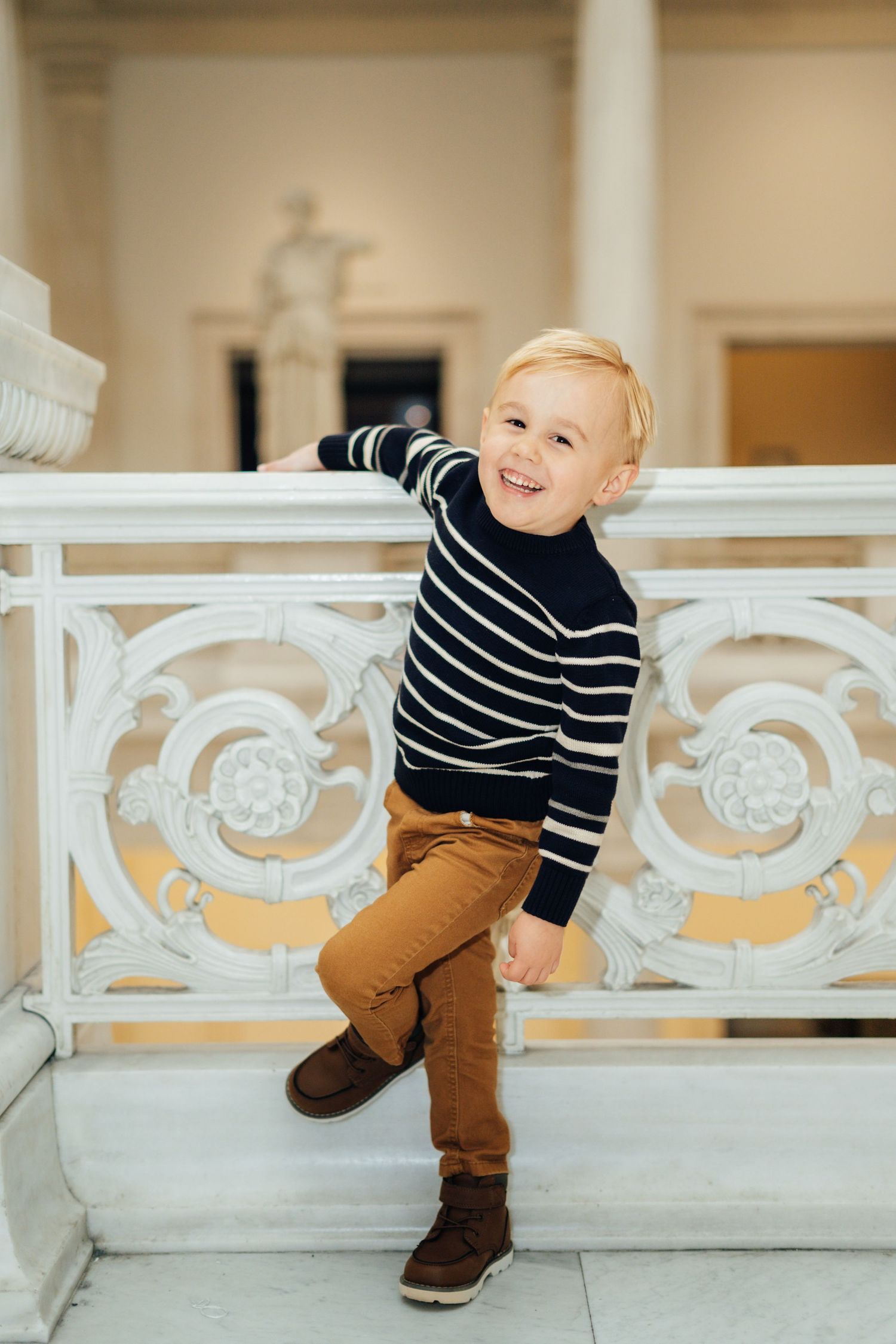 A toddler in striped sweater and brown pants plays along a decorative white railing in a sequence of photos.