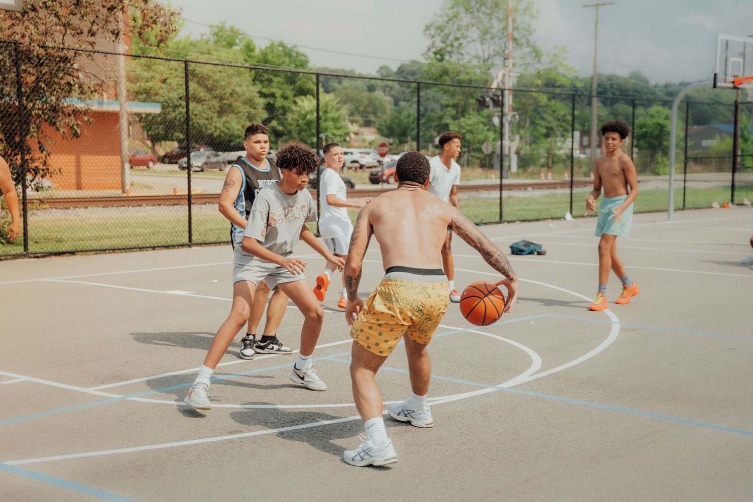 Group of friends playing a casual game of basketball on an outdoor court during a warm summer day.