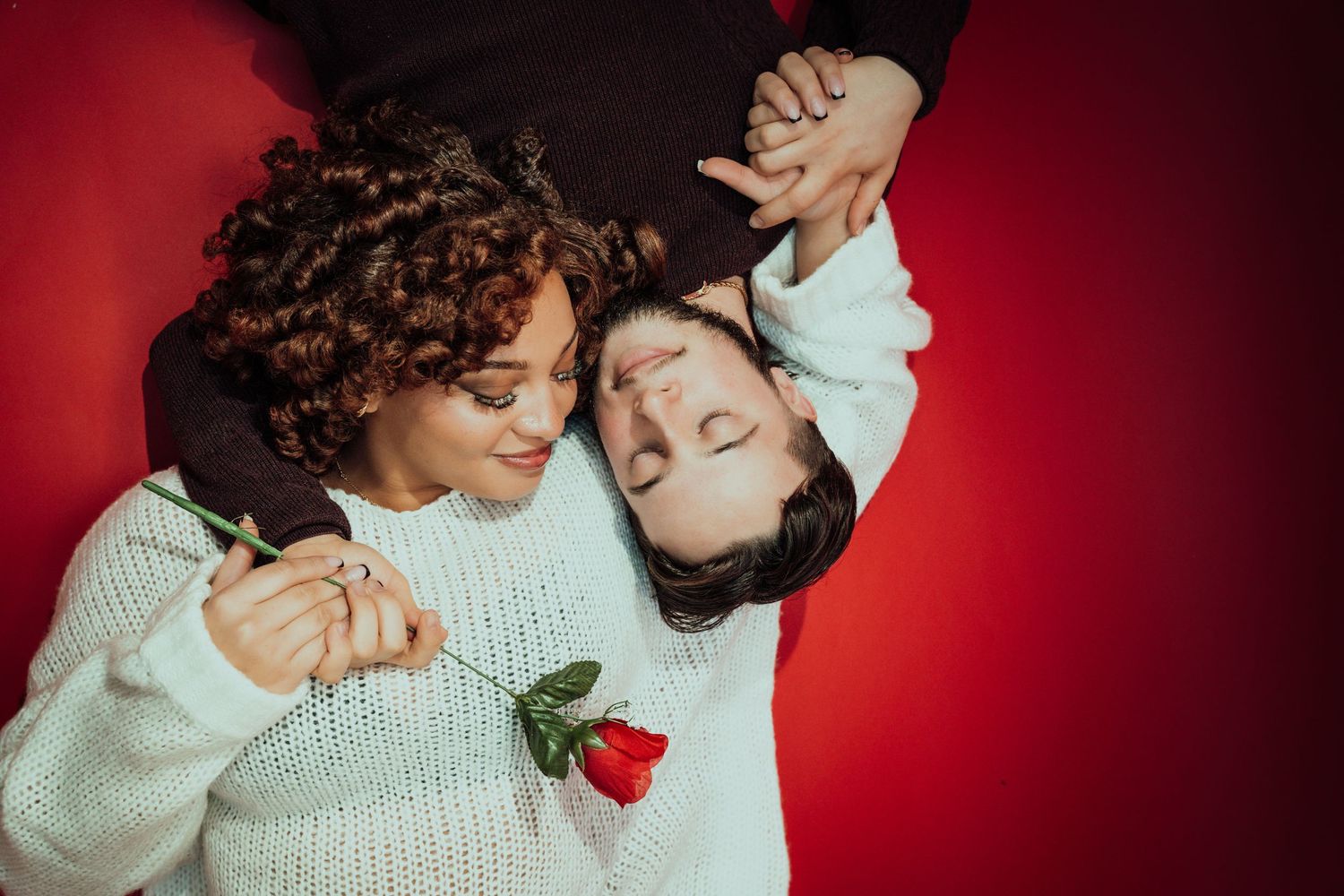 Artistic overhead shot of two people with red rose against vibrant red backdrop.
