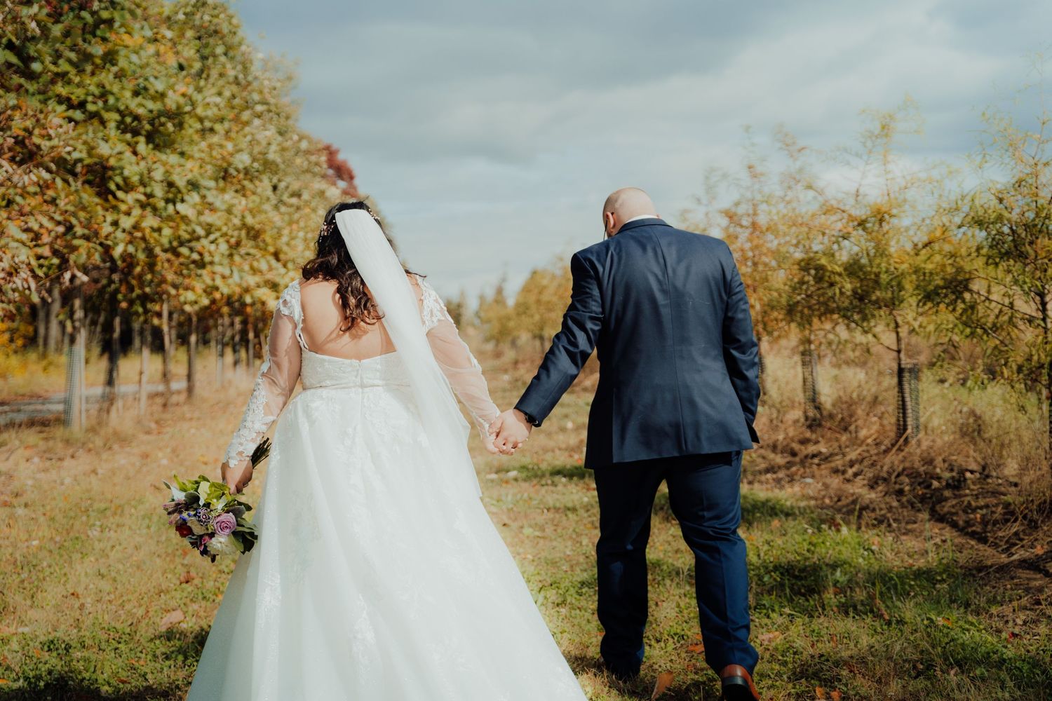 Bride and groom walking together through a sun-drenched autumn field.