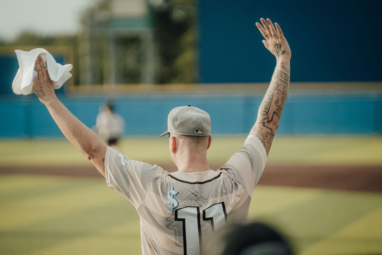 Baseball player celebrates with raised arms after scoring winning run on sunny field during game.