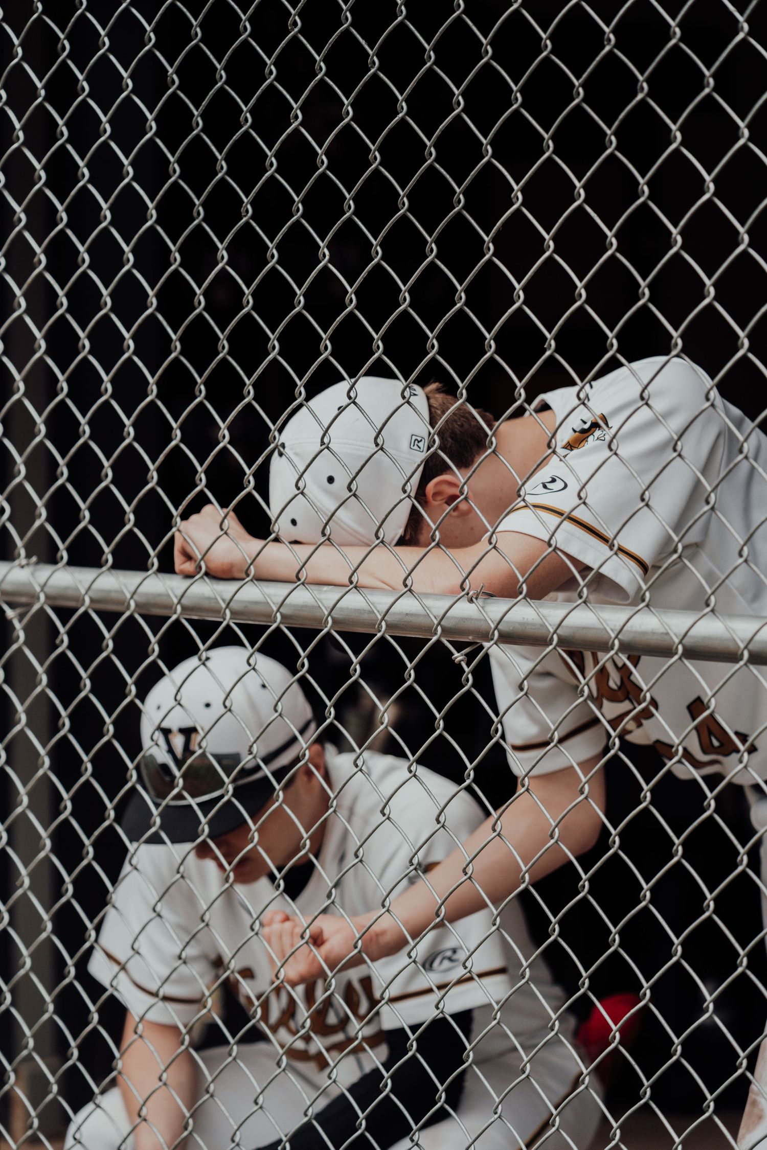 Baseball players in white uniforms seen through chain link fence during game.
