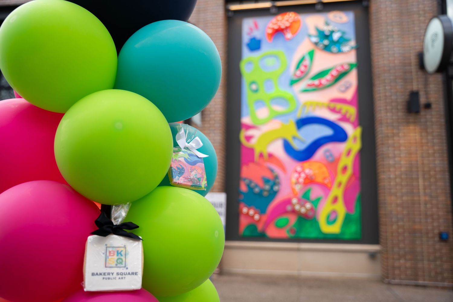 Colorful balloons in front of a vibrant mural display on a brick building wall.