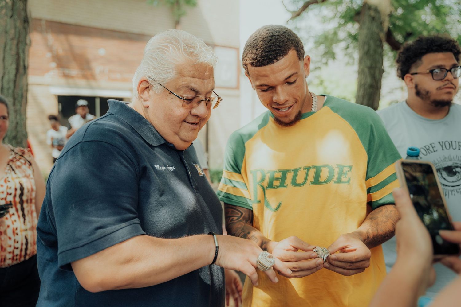 Two people look at a mobile device together outdoors while wearing casual clothing.