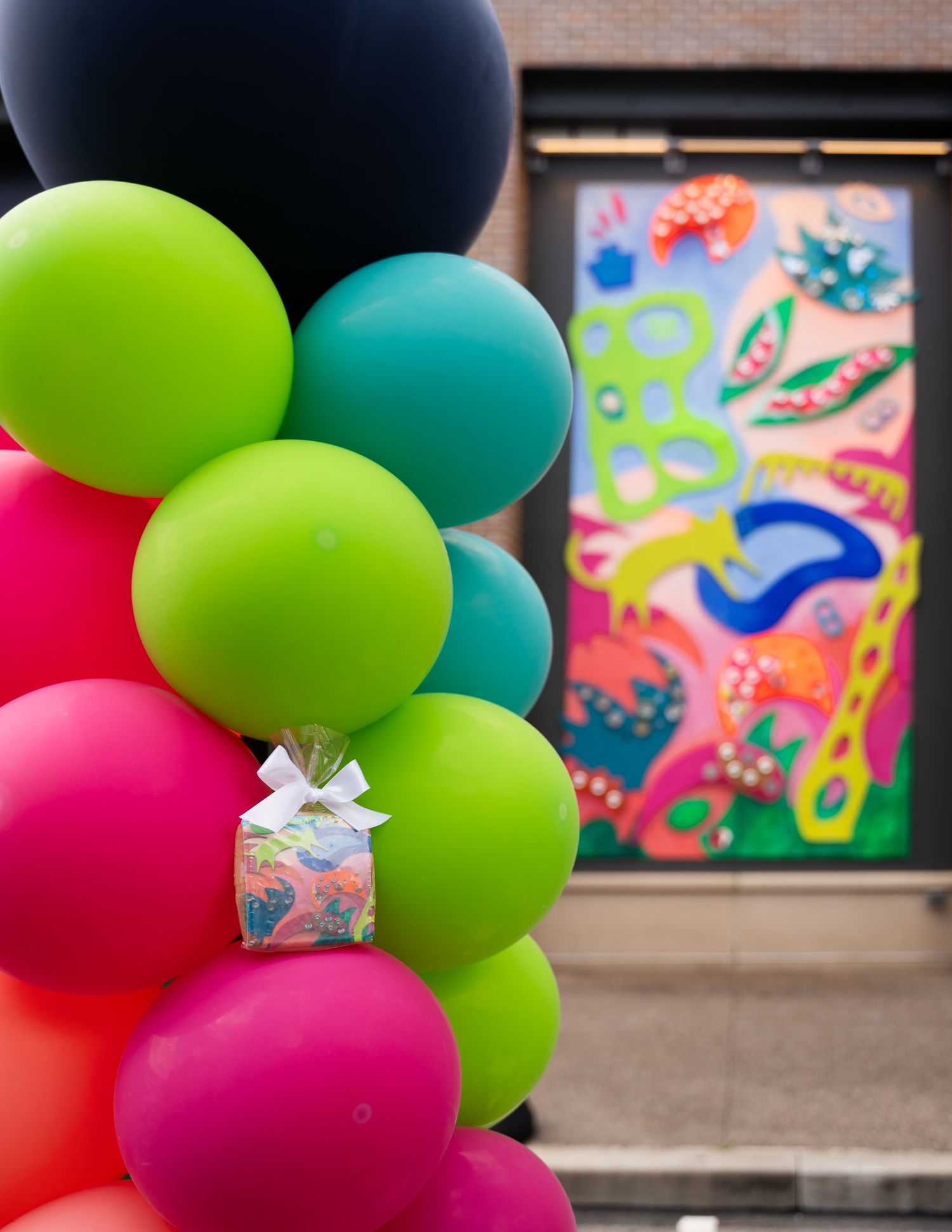 Colorful balloons in pink, green, and teal arranged against a dark background with abstract art.