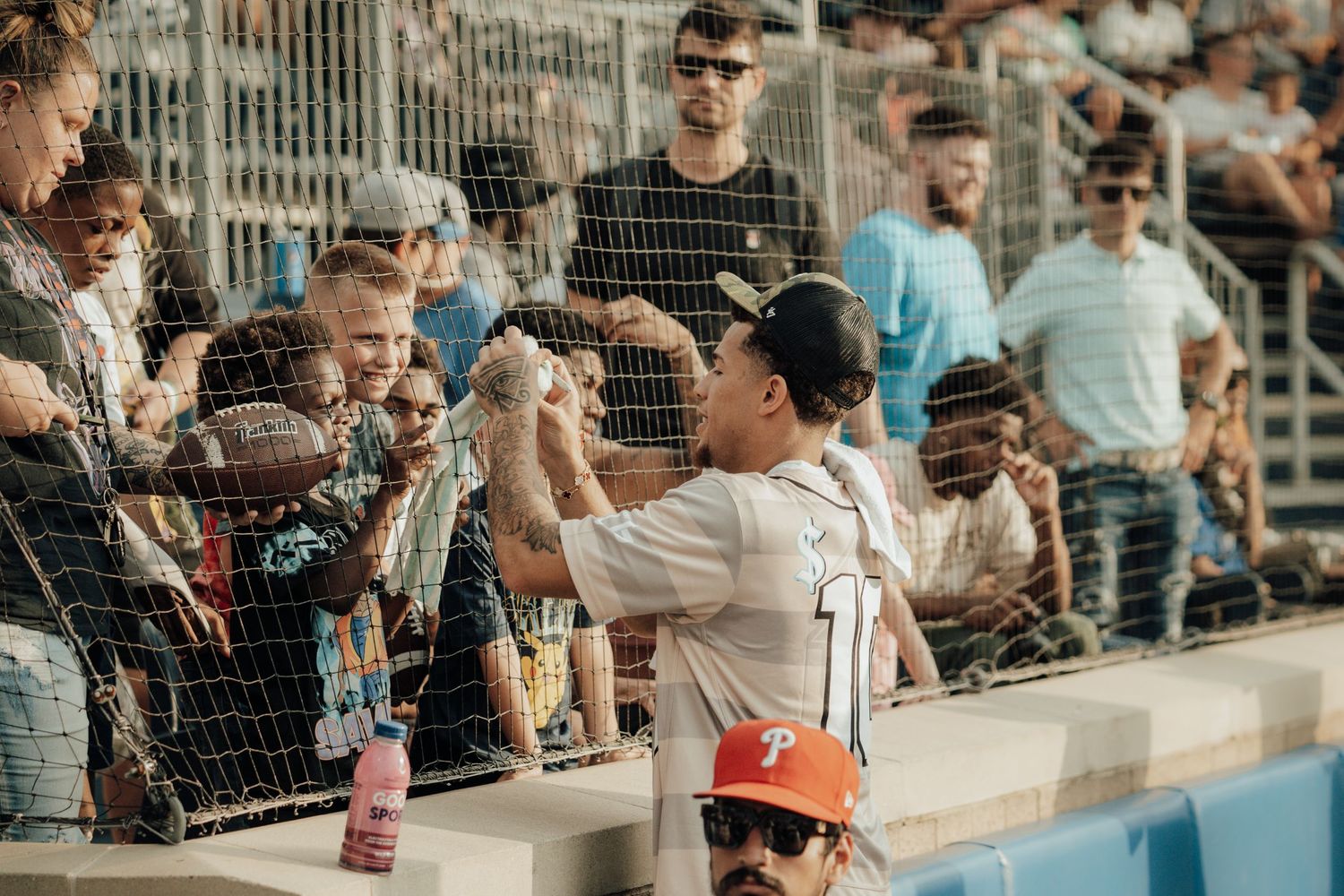 Baseball player wearing white jersey interacts with young fan through protective fence during game.
