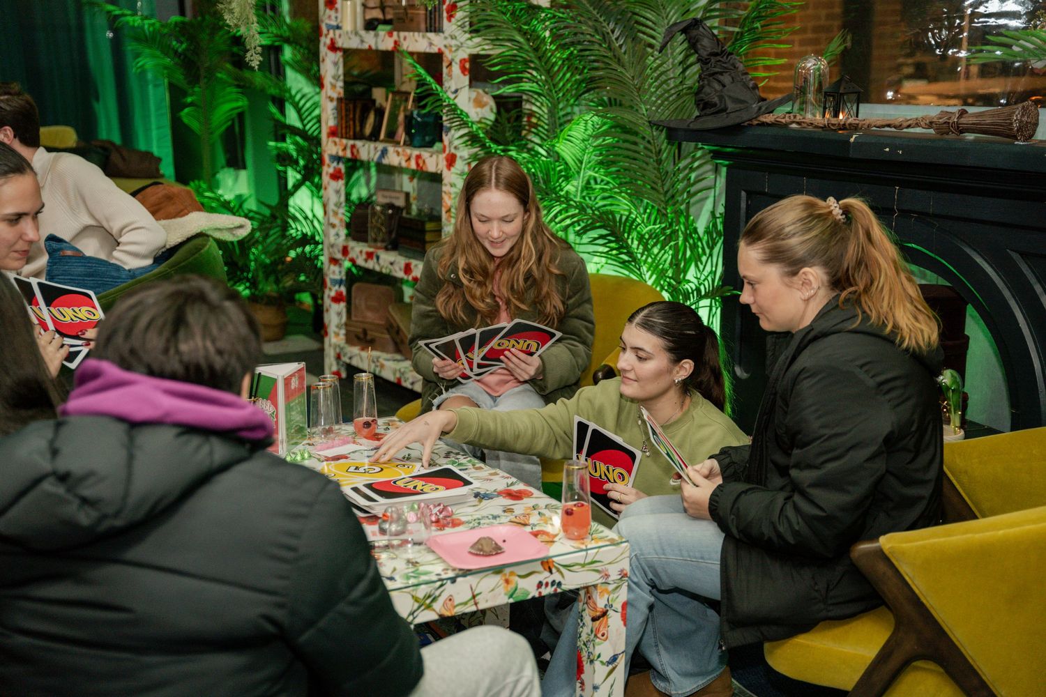 People sitting at a table with festive decor playing cards or board games in a cozy restaurant with green lighting.