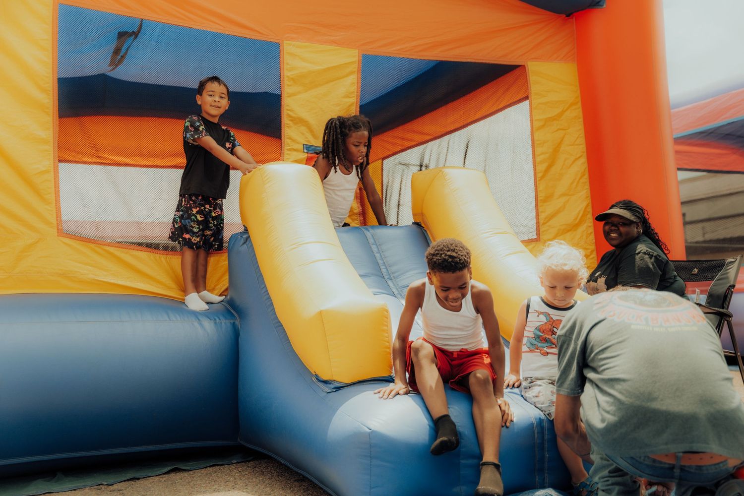 Kids play and bounce inside a colorful inflatable bounce house with yellow, blue and orange sections.