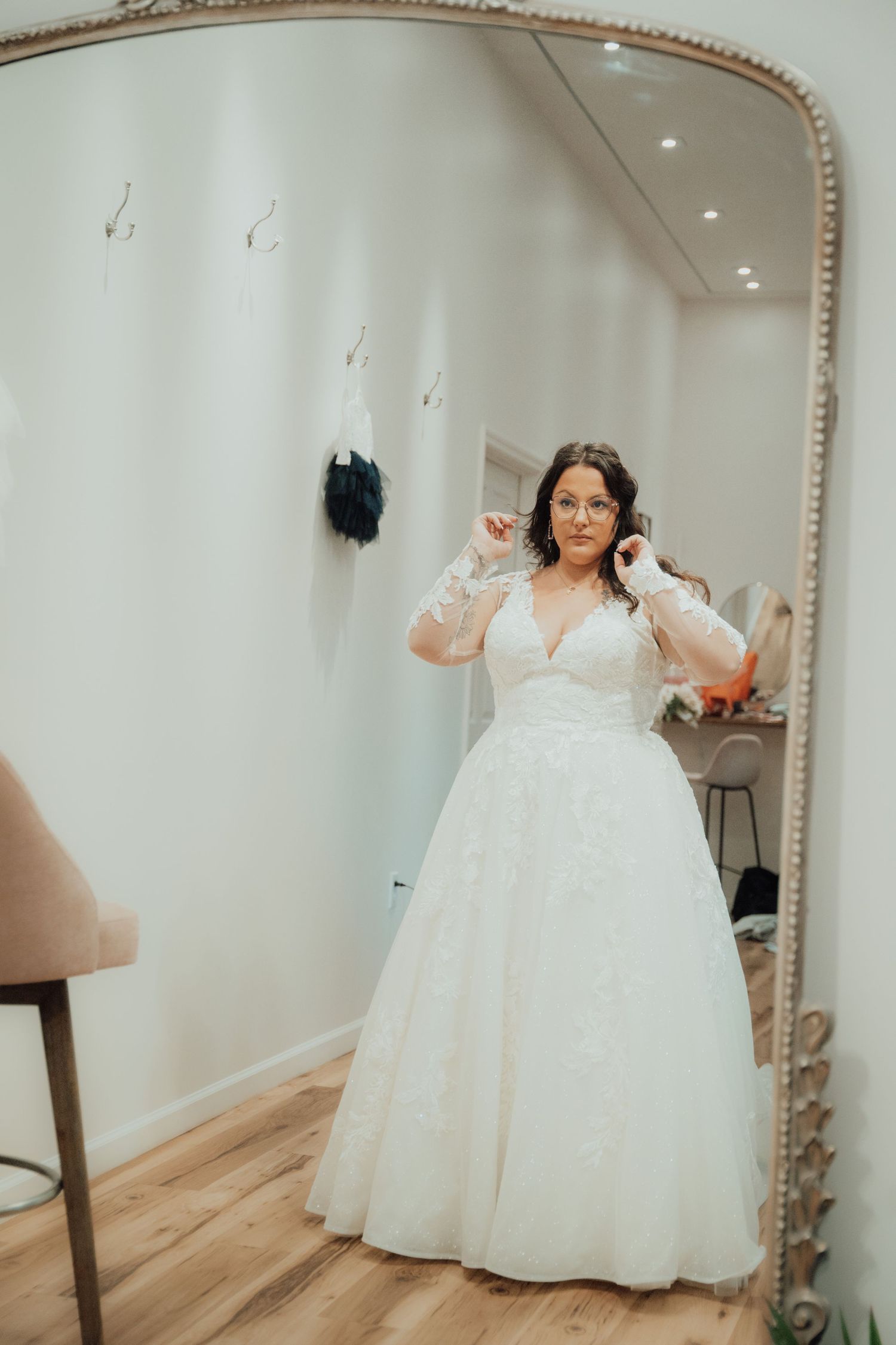 Bride in beautiful white ballgown adjusting earrings in ornate mirror.