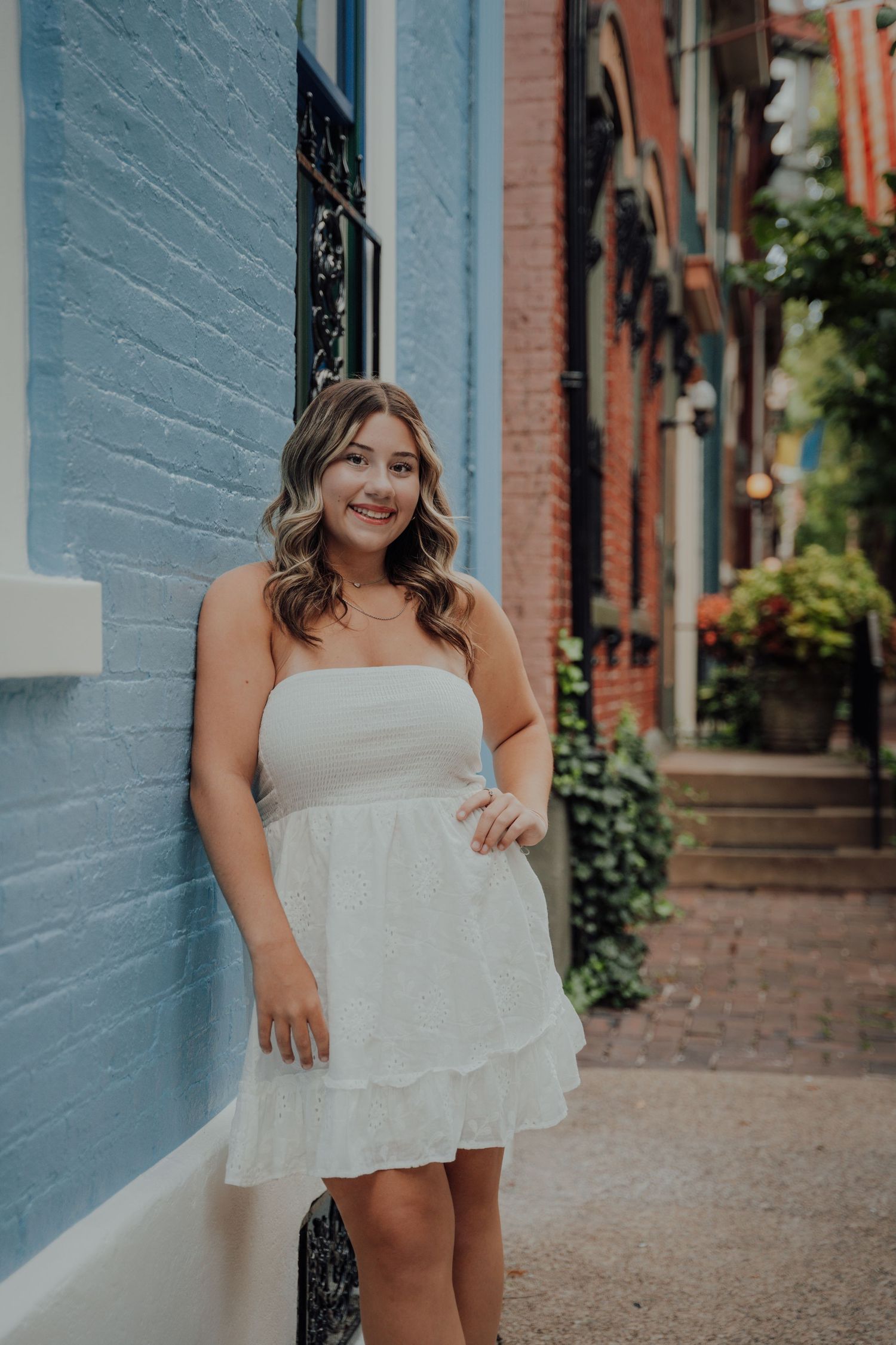 Portrait series against blue brick wall capturing joyful expressions in white dress.
