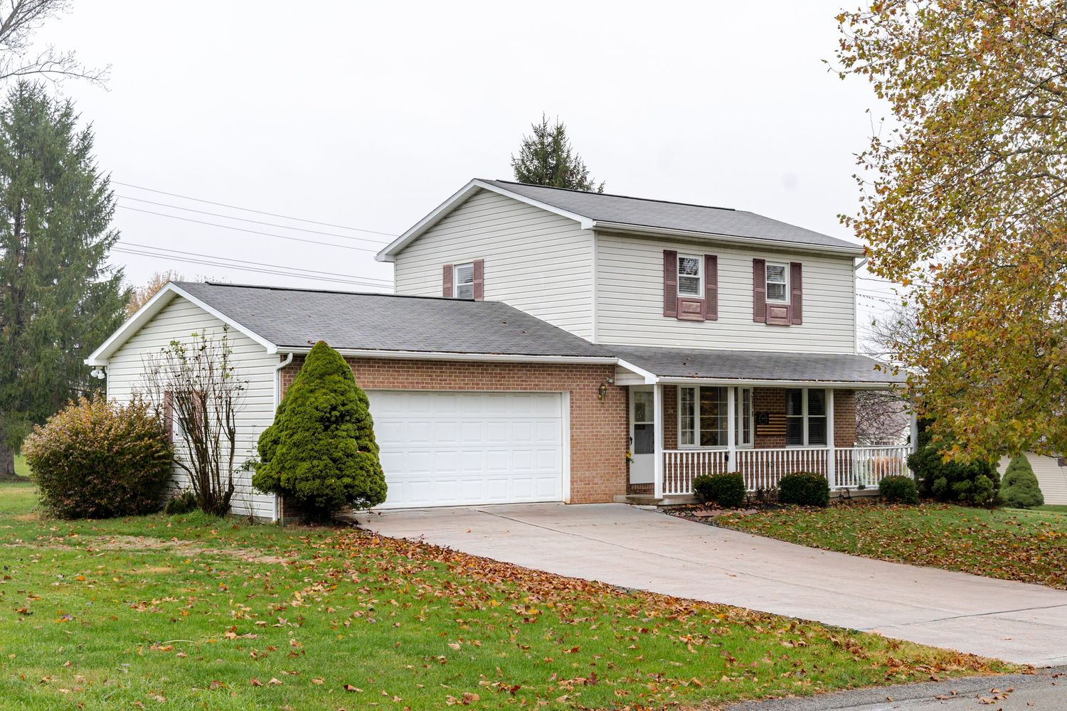 A white ranch-style house with attached garage and landscaped yard in autumn with trees showing fall colors.