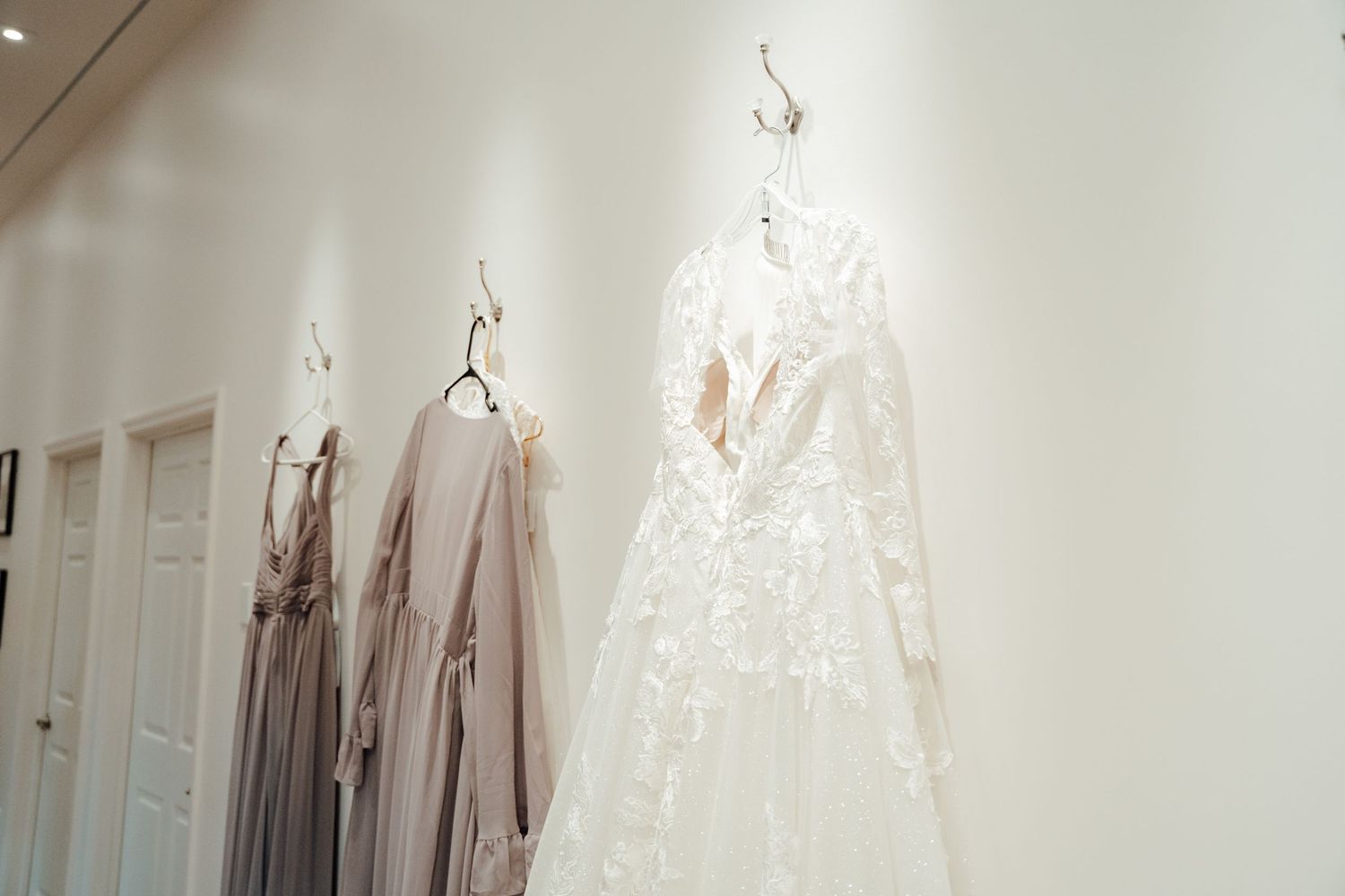Wedding dresses displayed on white wall with bridesmaid gowns in soft neutral tones.