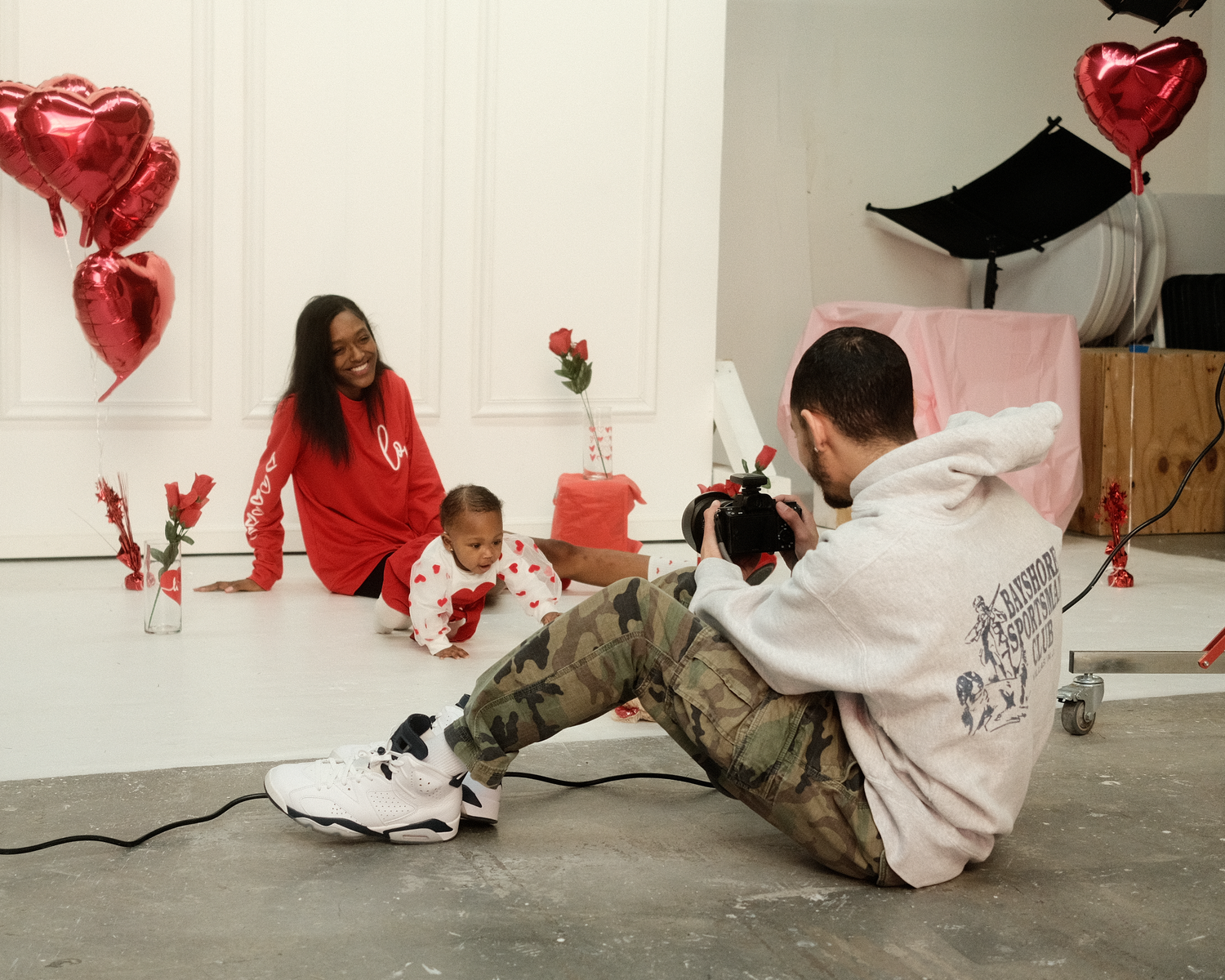 Family photo shoot setup with red heart balloons and white backdrop.