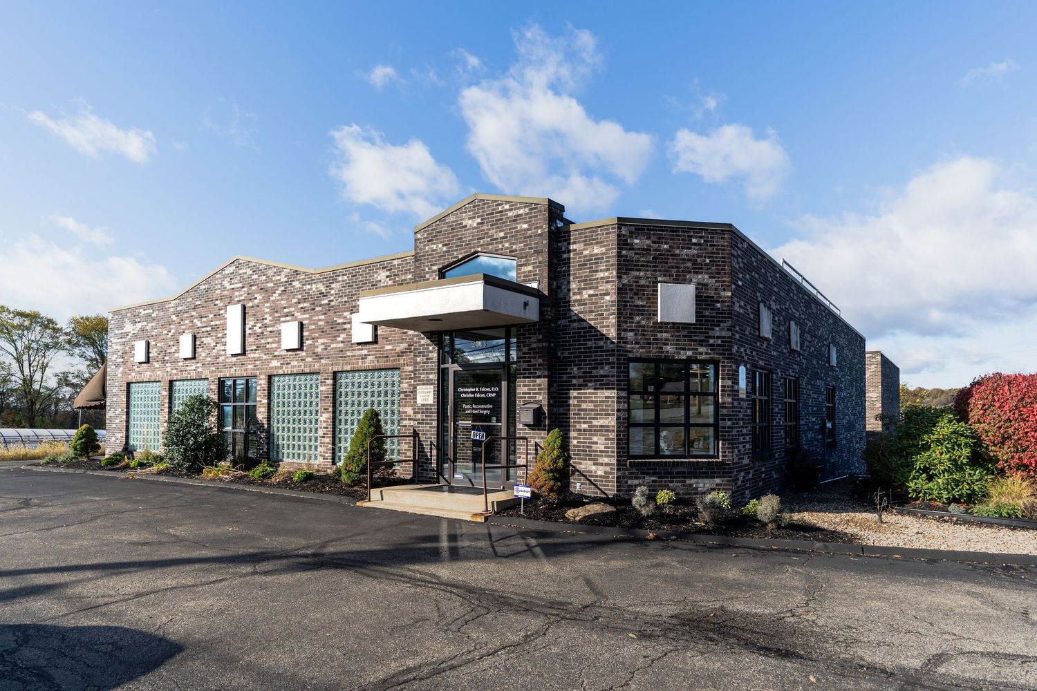 Modern office building exterior with brick facade and large windows shown in a panoramic view under blue sky.