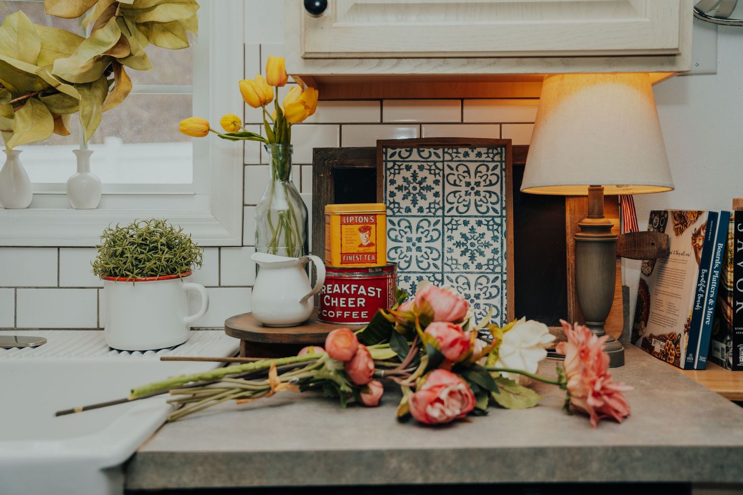 Cozy kitchen counter vignette with warm lighting, decorative flowers, and vintage-inspired home decor elements.