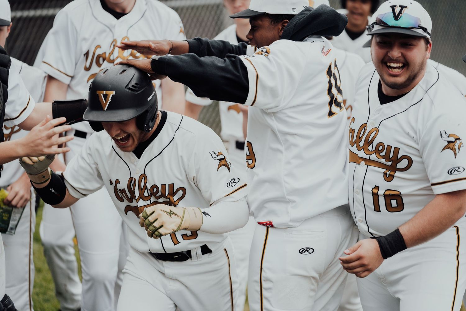 Baseball team celebrates with high fives and excitement in the dugout.