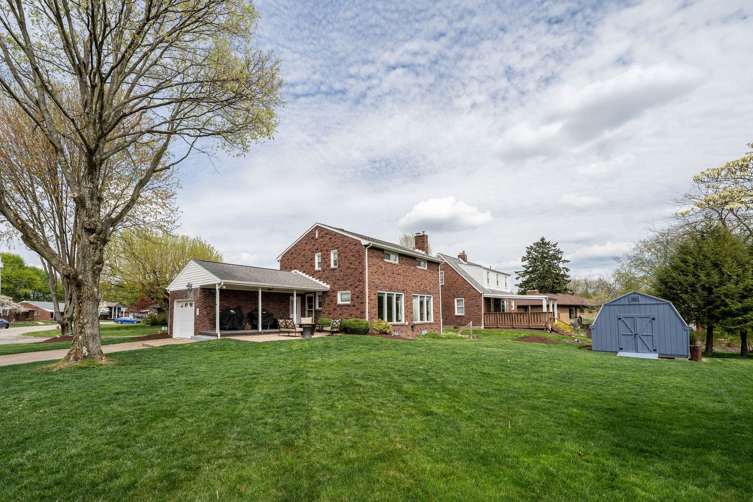 Panoramic view of a rural property with brick homes and outbuildings nestled among green rolling hills on a spring day.
