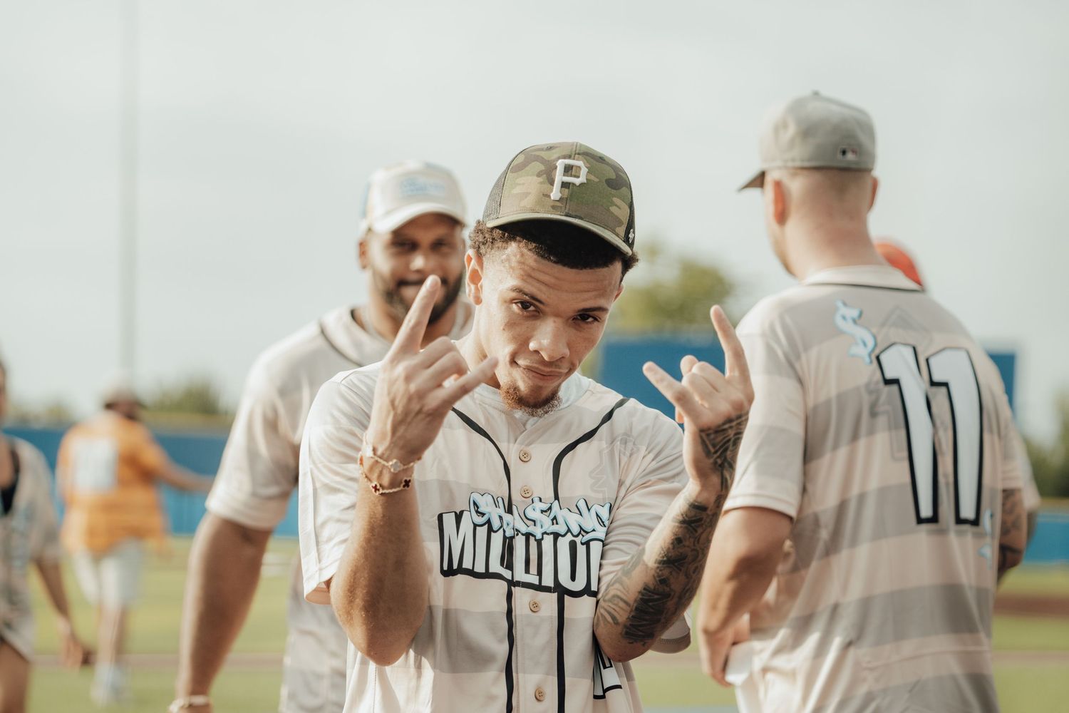 Baseball players in white uniforms gather on field during recreational league game on sunny afternoon.