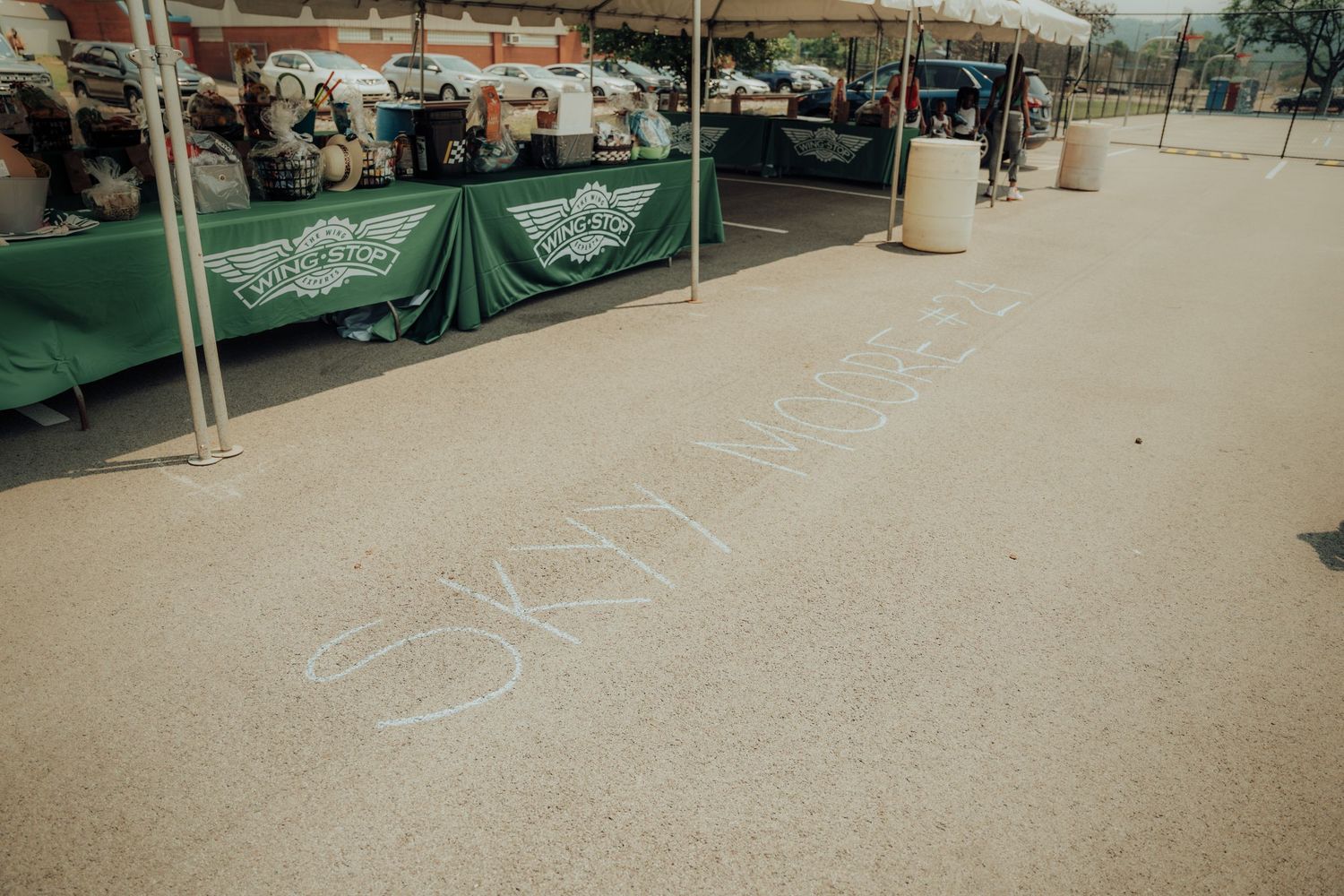 Words written in chalk on concrete ground near green vendor tents at an outdoor market or event setup.