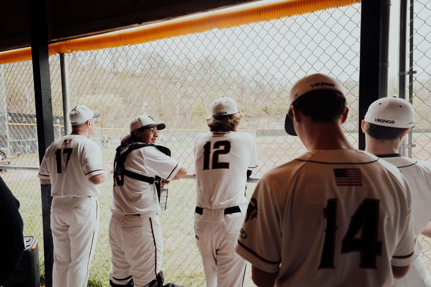 Baseball players gather in dugout during game wearing white uniforms.