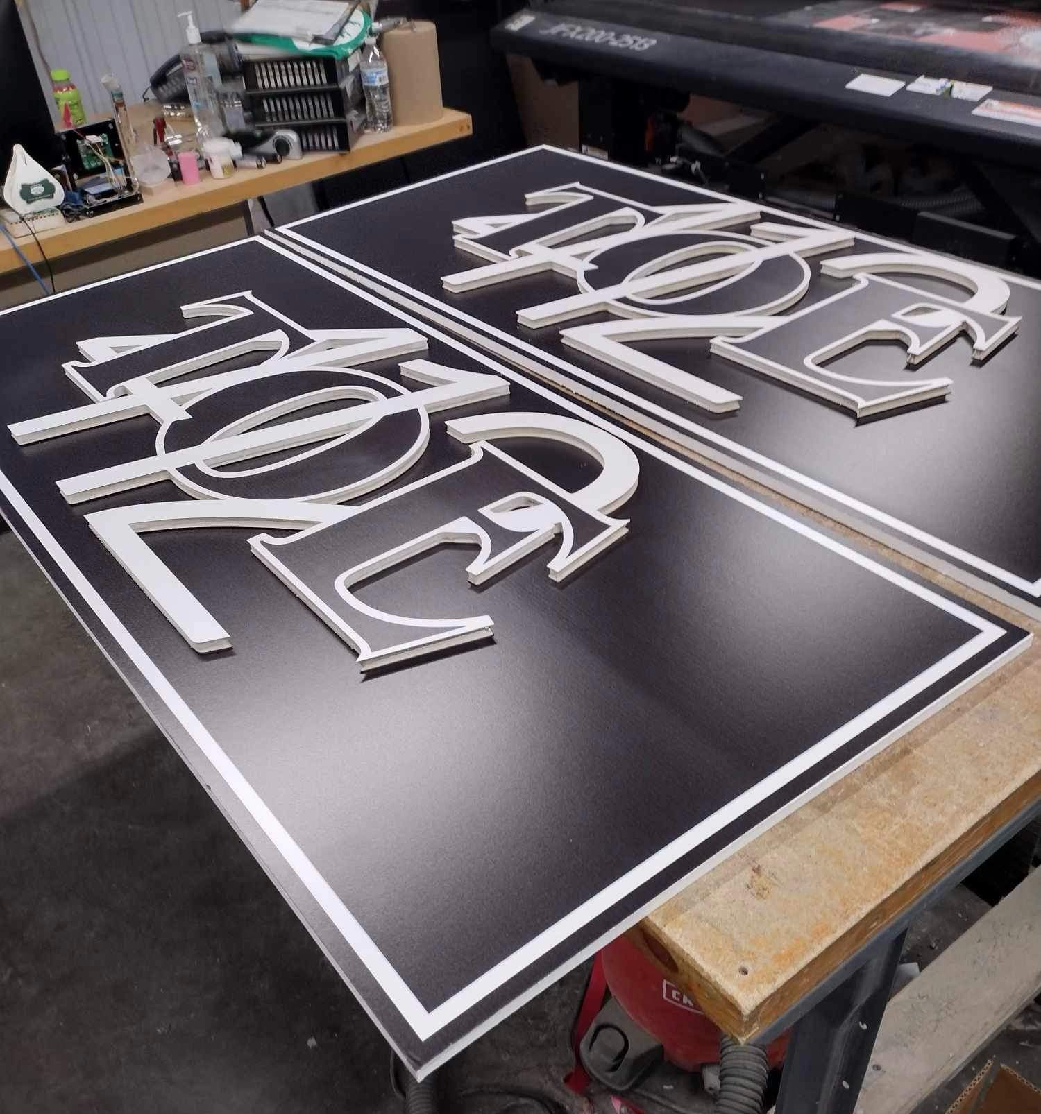 Time lapse photos showing the fabrication process of a large dimensional black and white sign panel on a workbench.