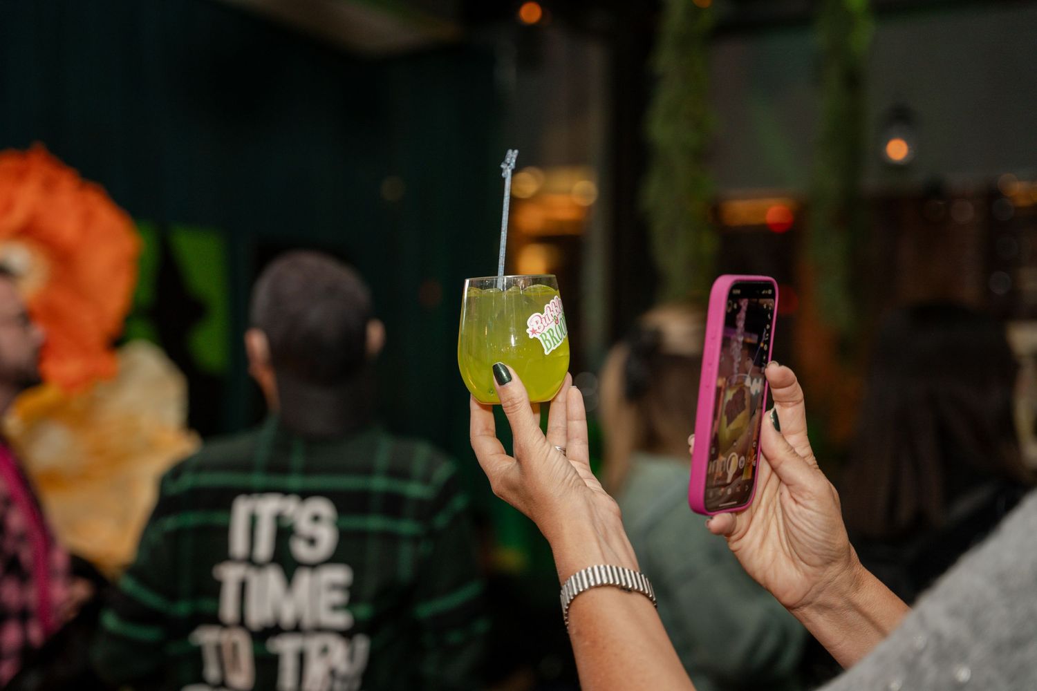 People holding phones at a social gathering with green lighting effects.