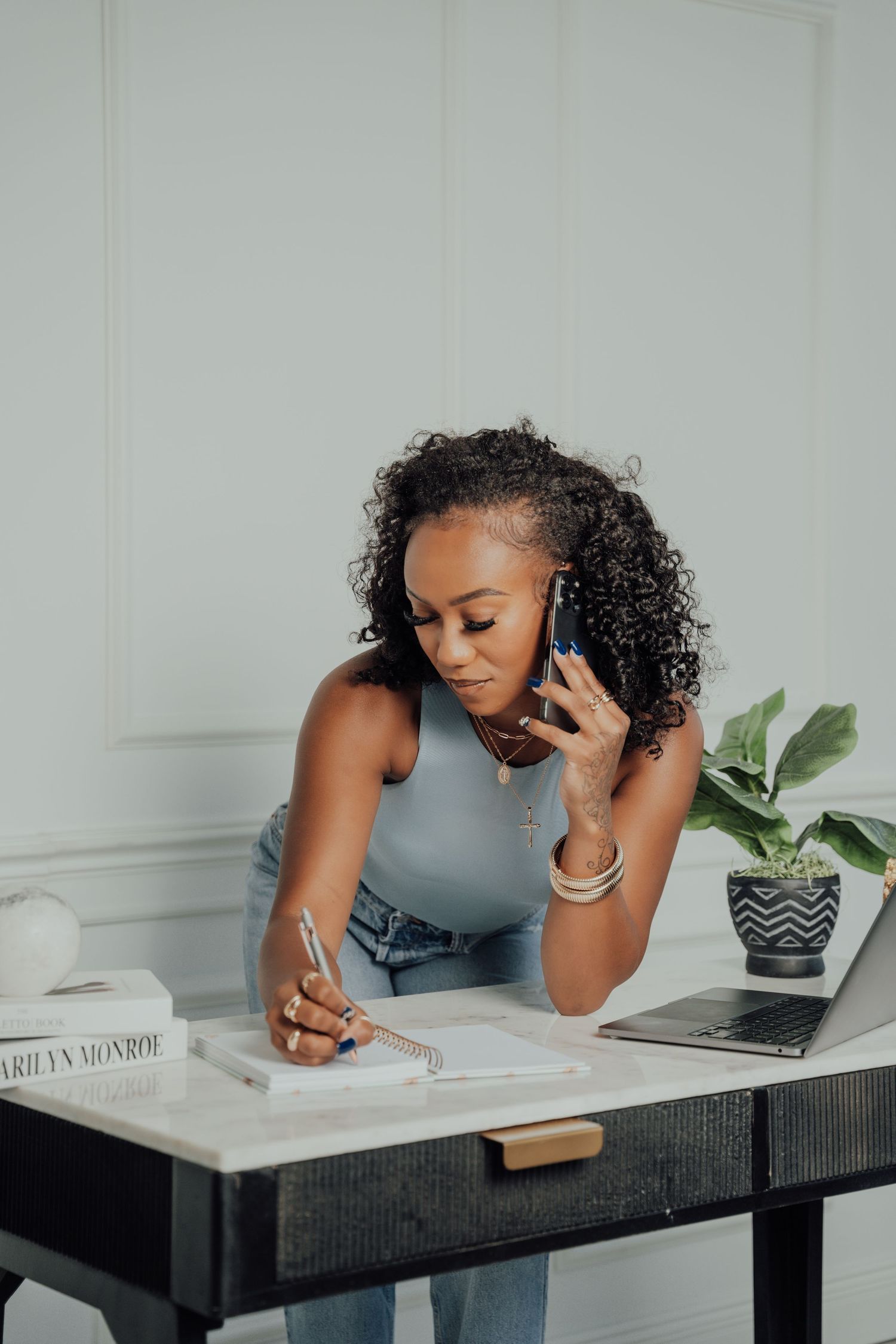 Woman in gray top working at desk with laptop and taking notes.