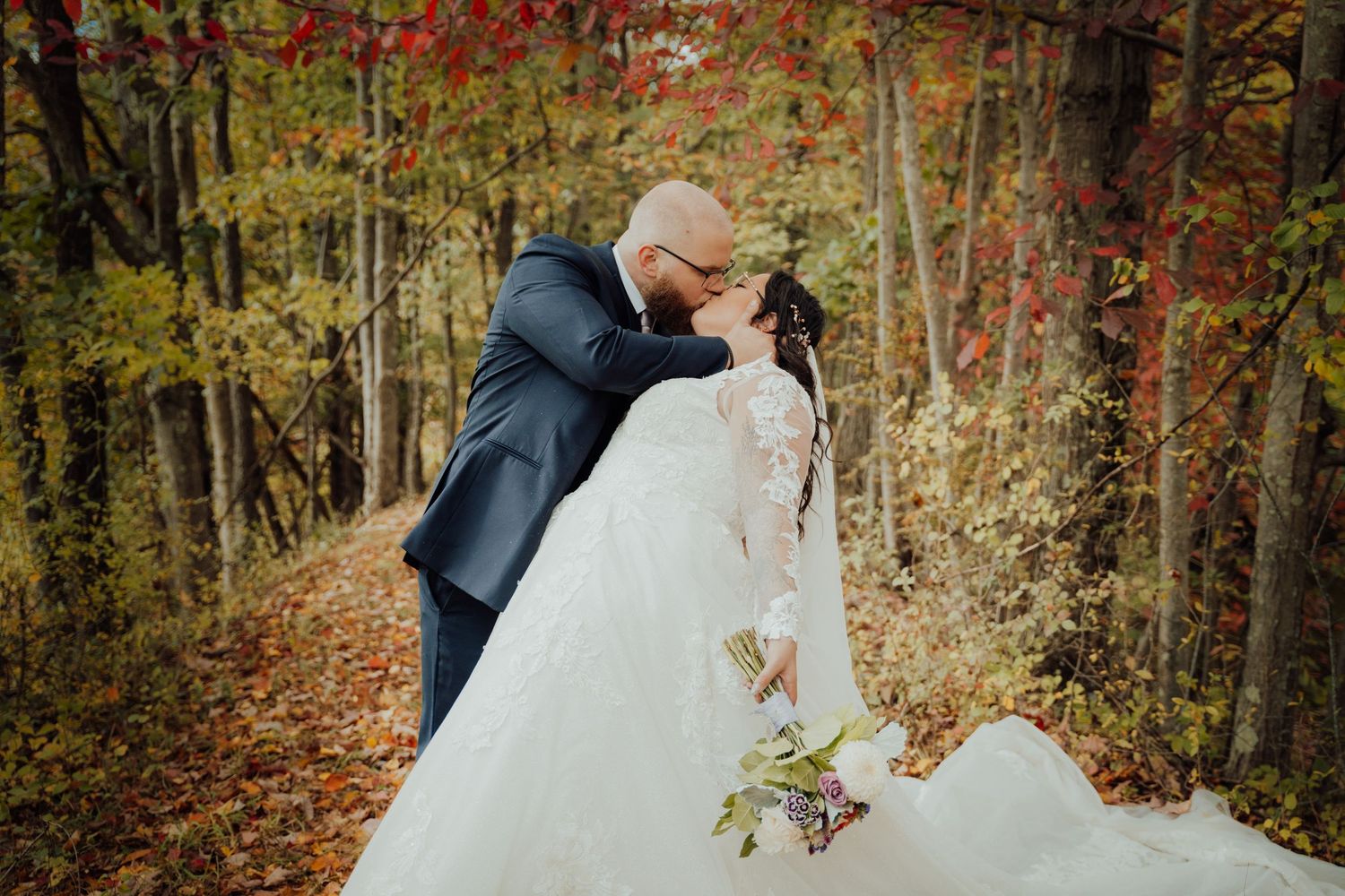 Wedding couple sharing intimate moments among vibrant fall foliage.