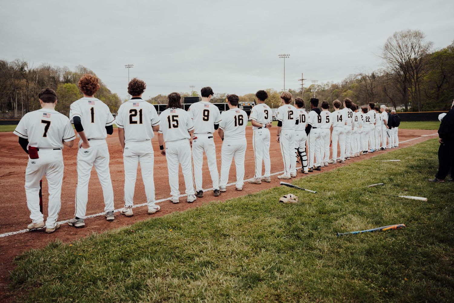 Baseball team lined up along field showing jersey numbers on their white uniforms.