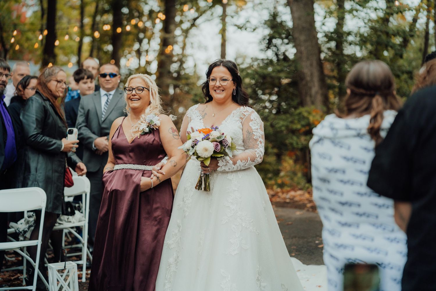 Joyful outdoor wedding ceremony with smiling bride walking down aisle in autumn setting.