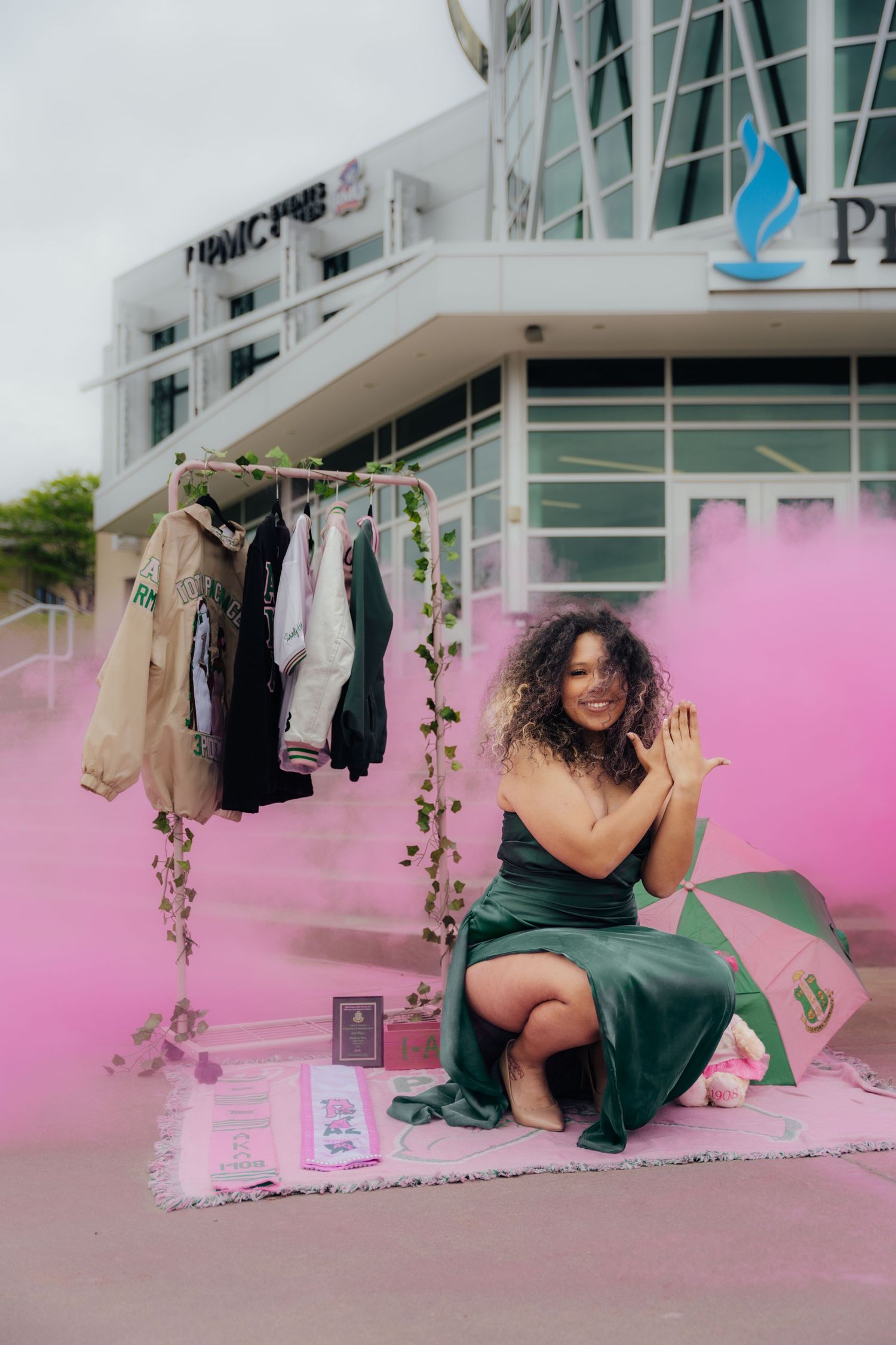 Creative fashion photoshoot with pink smoke and hanging clothes rack against white building exterior.