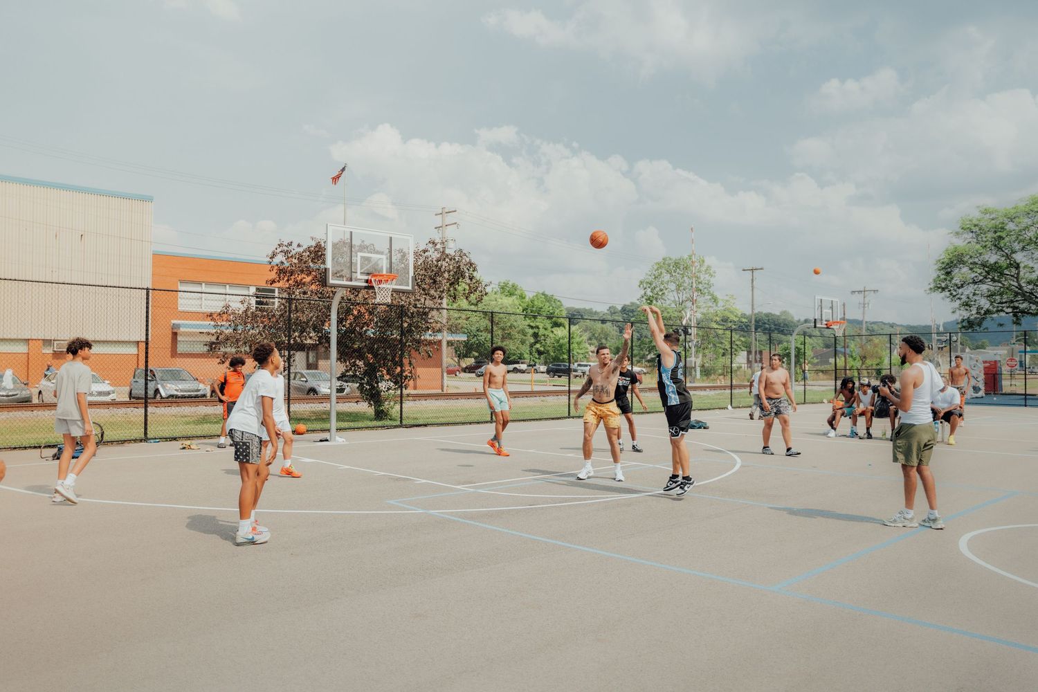 A group plays basketball on an outdoor court during a sunny day with players dribbling and passing the ball.