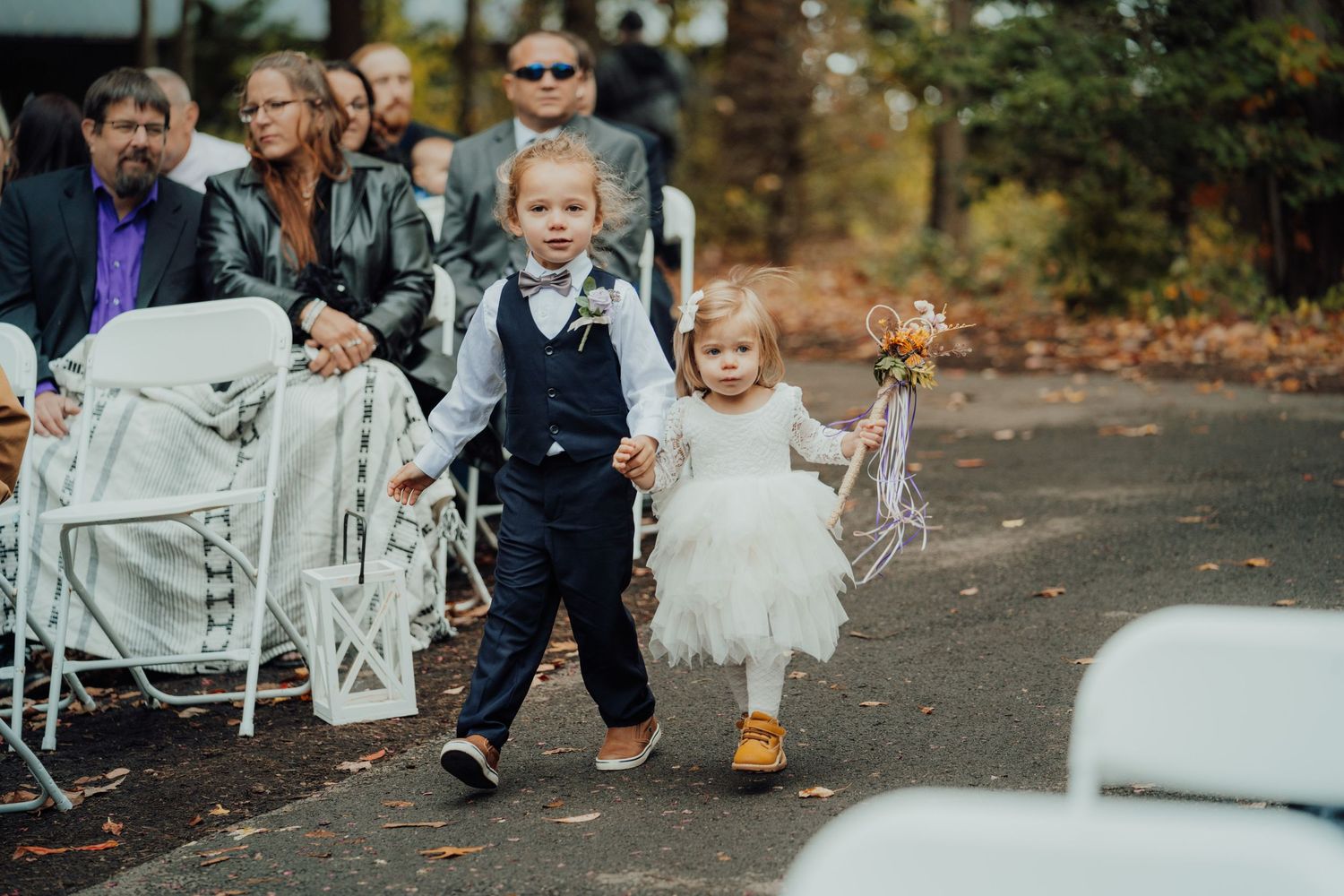 Wedding guests gathering at an outdoor ceremony with white chairs and fall leaves.