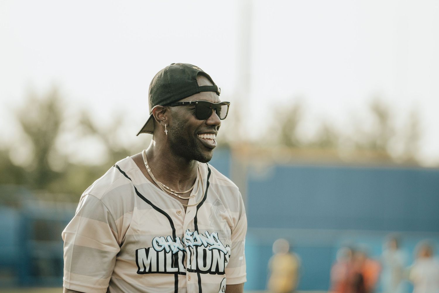 A baseball player wearing a Miami uniform smiles while wearing glasses and a backwards cap during a sunny game.