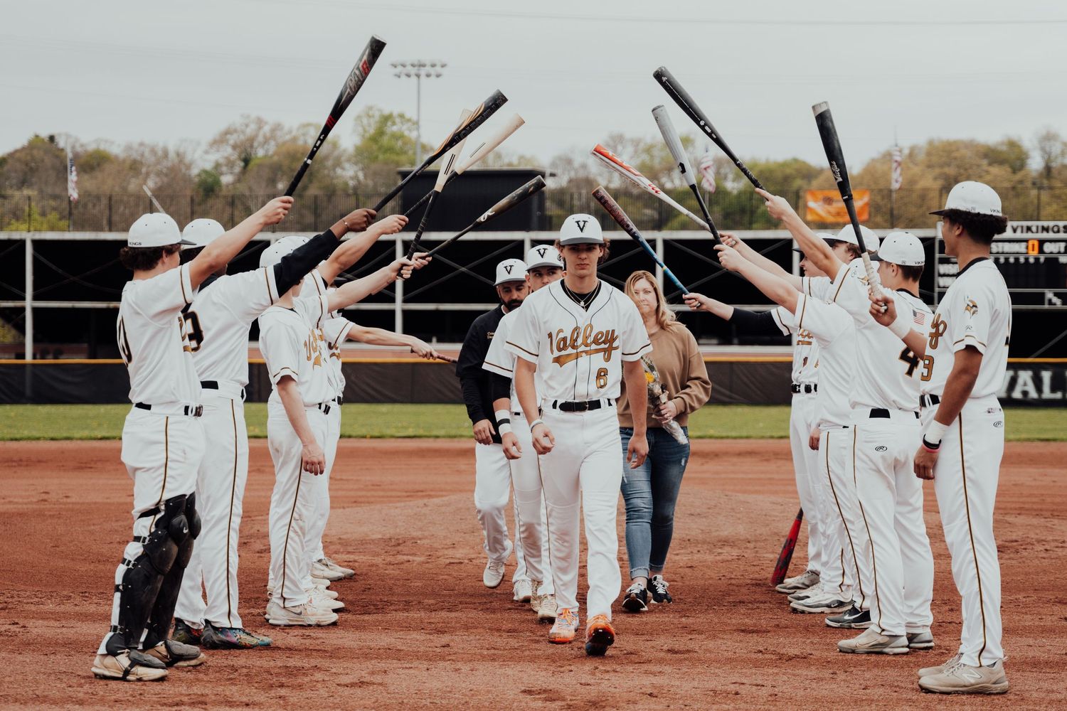 Baseball players line up in white uniforms forming an archway with bats raised for a game tradition.