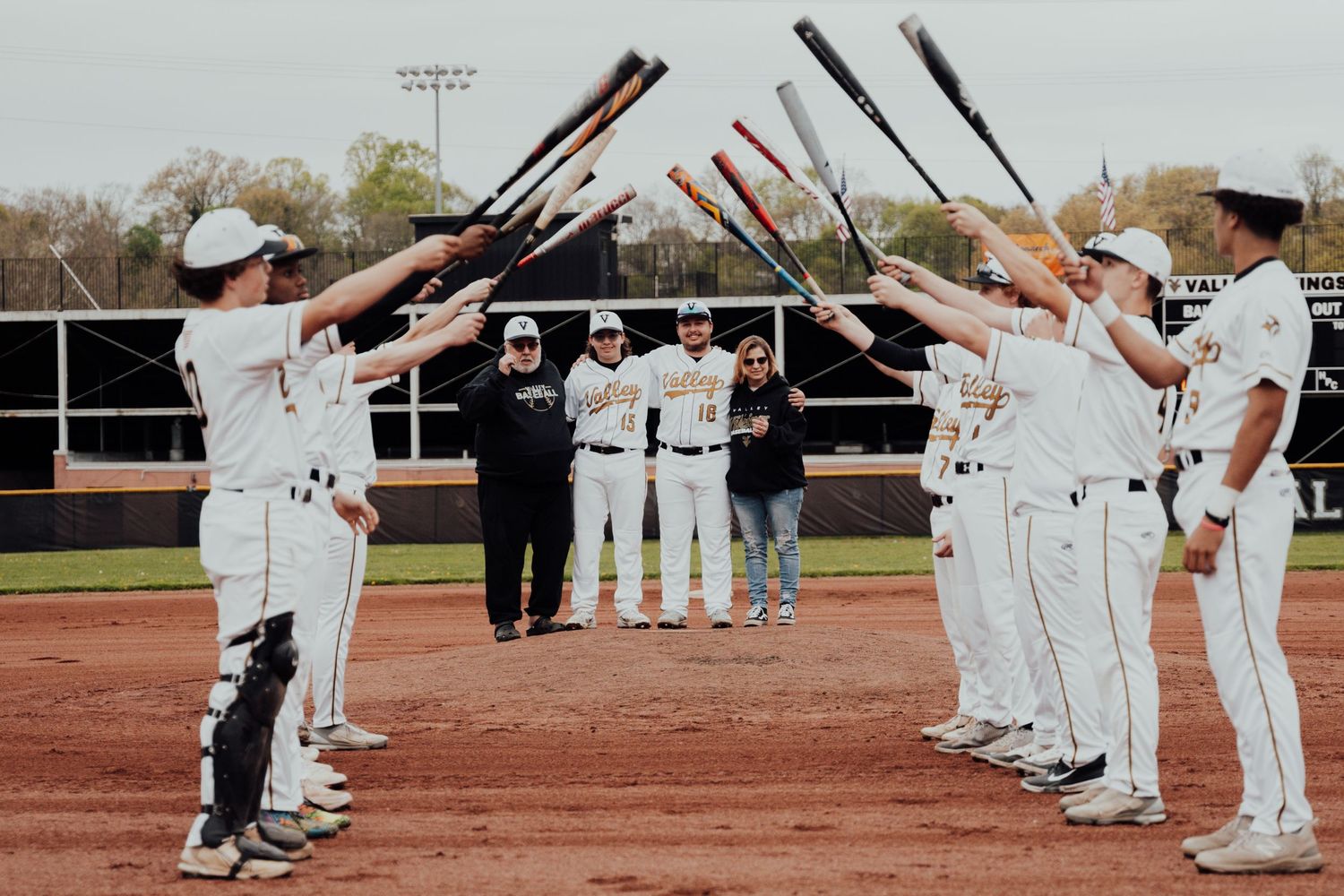Baseball team celebrates by creating an arch of baseball bats over their teammates walking beneath.