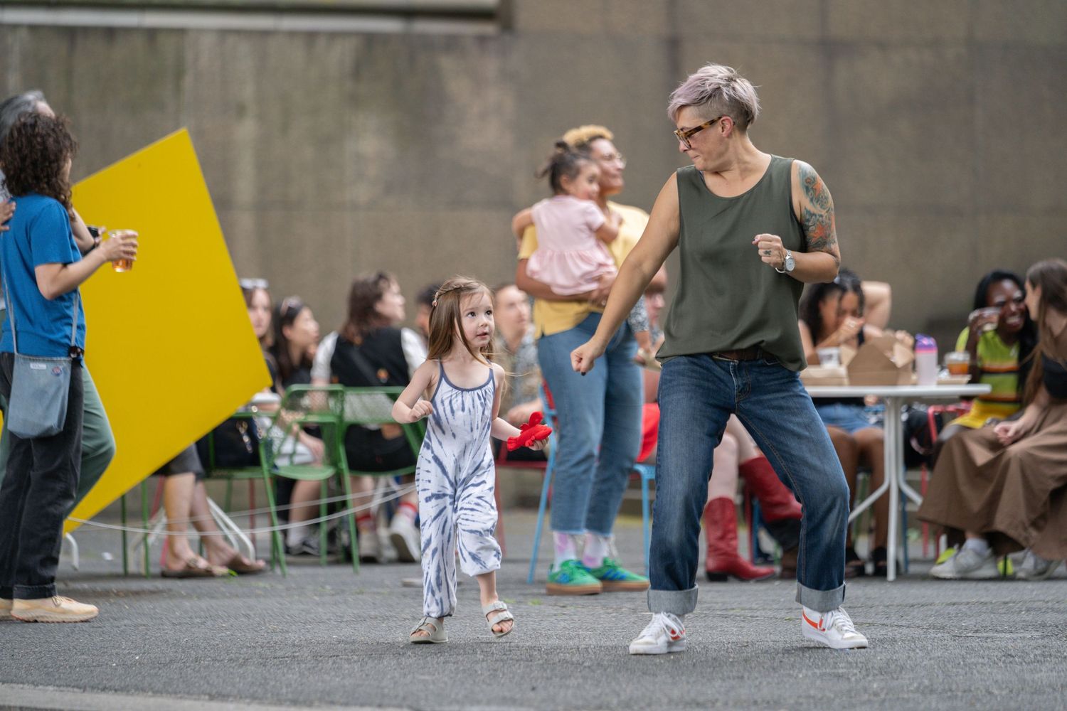 Event attendees mingling in an urban courtyard with yellow geometric installations.
