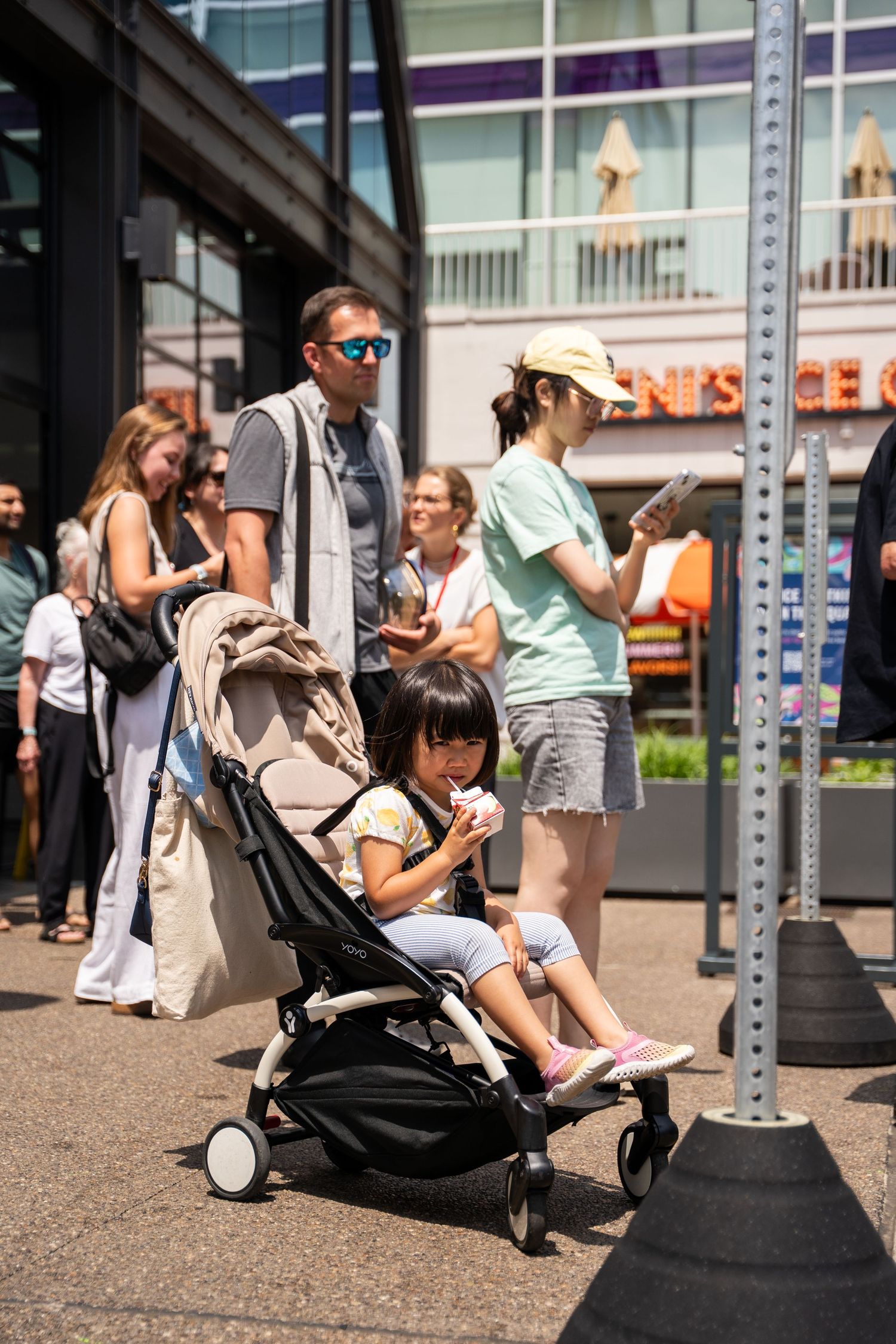 People sitting on curb near parking meter post on sunny urban sidewalk.